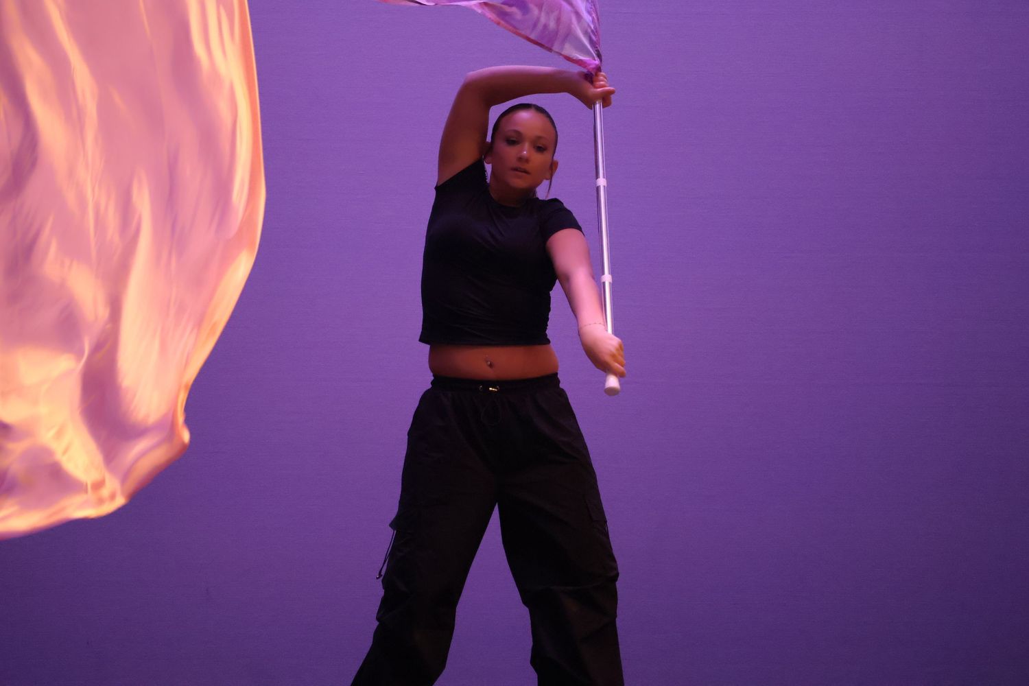 Performer with flag creates artistic movement against purple backdrop with orange lighting effects.