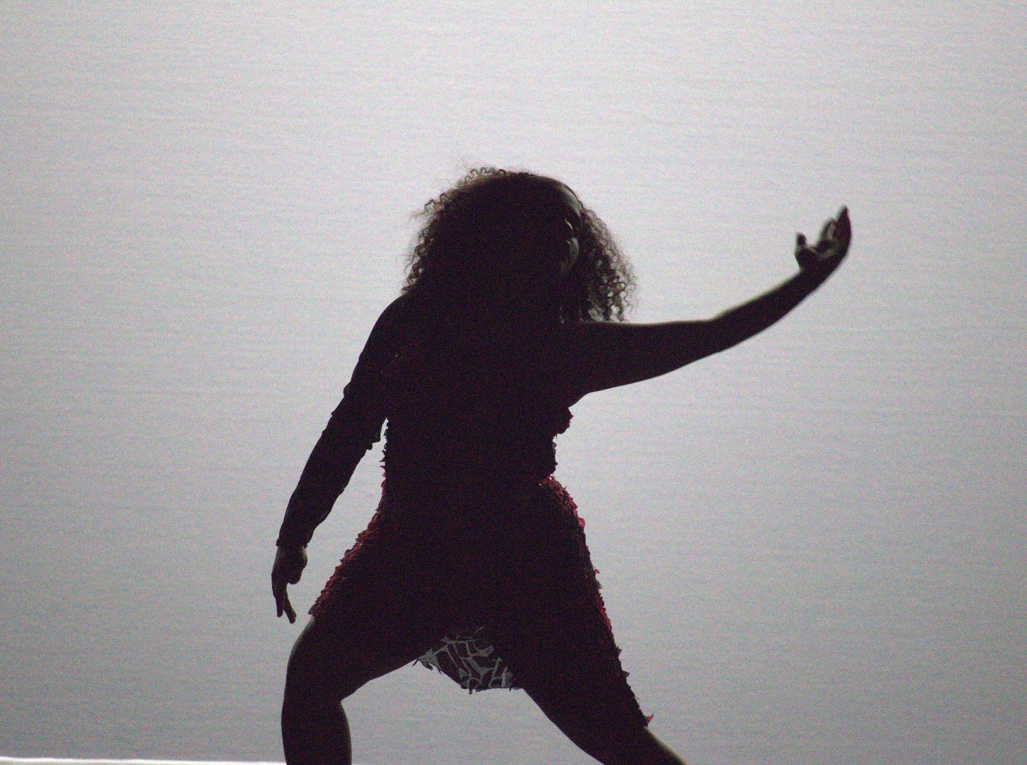 Silhouetted figure performs dynamic dance movements against light gray background.