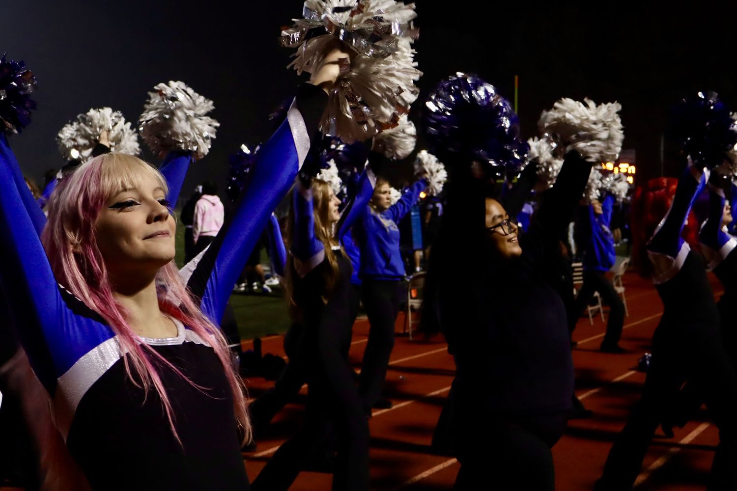 Dance team performs routine with blue pom poms during nighttime show.