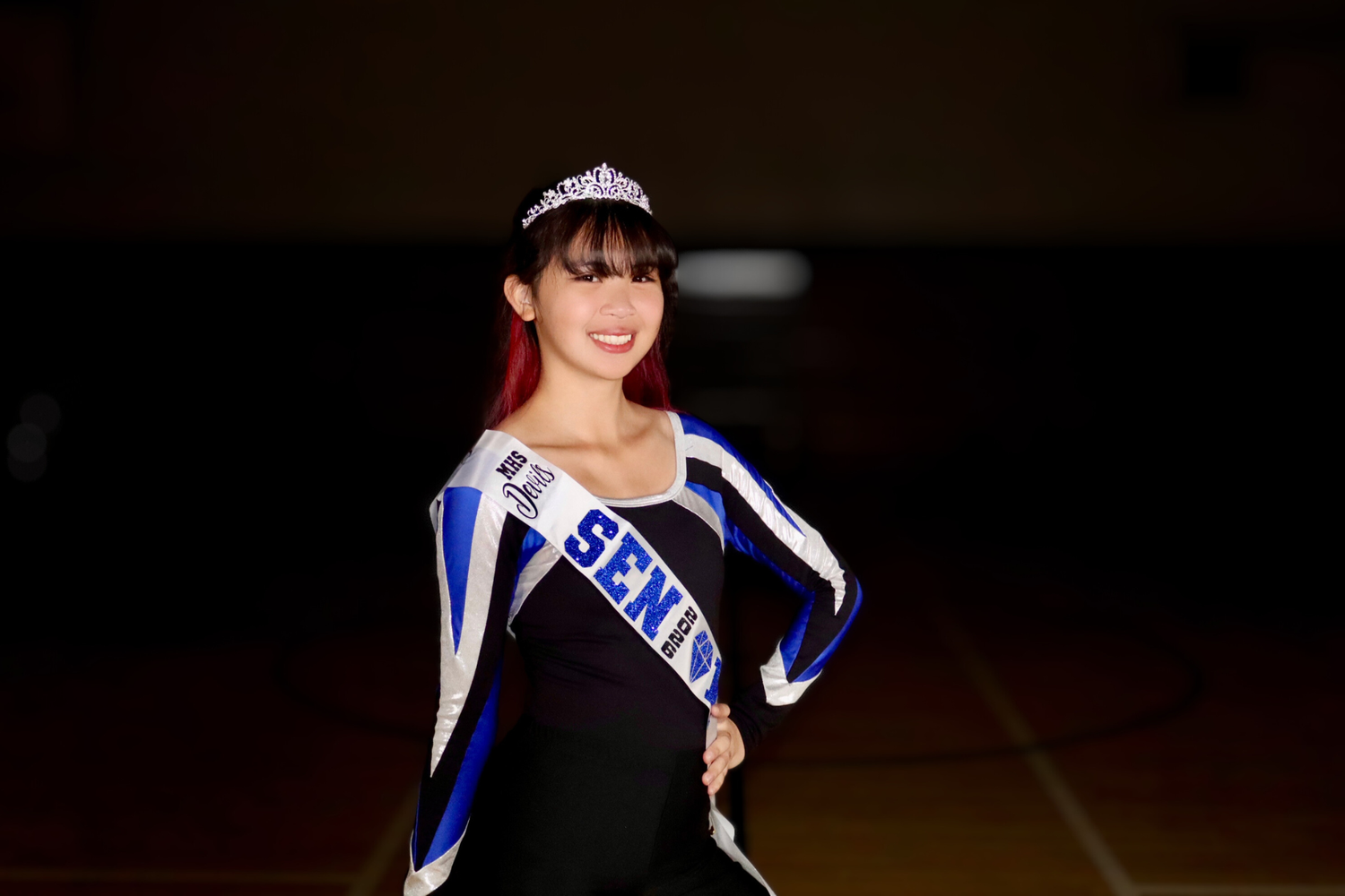 Performers in blue and white uniforms pose with crowns under dramatic lighting.