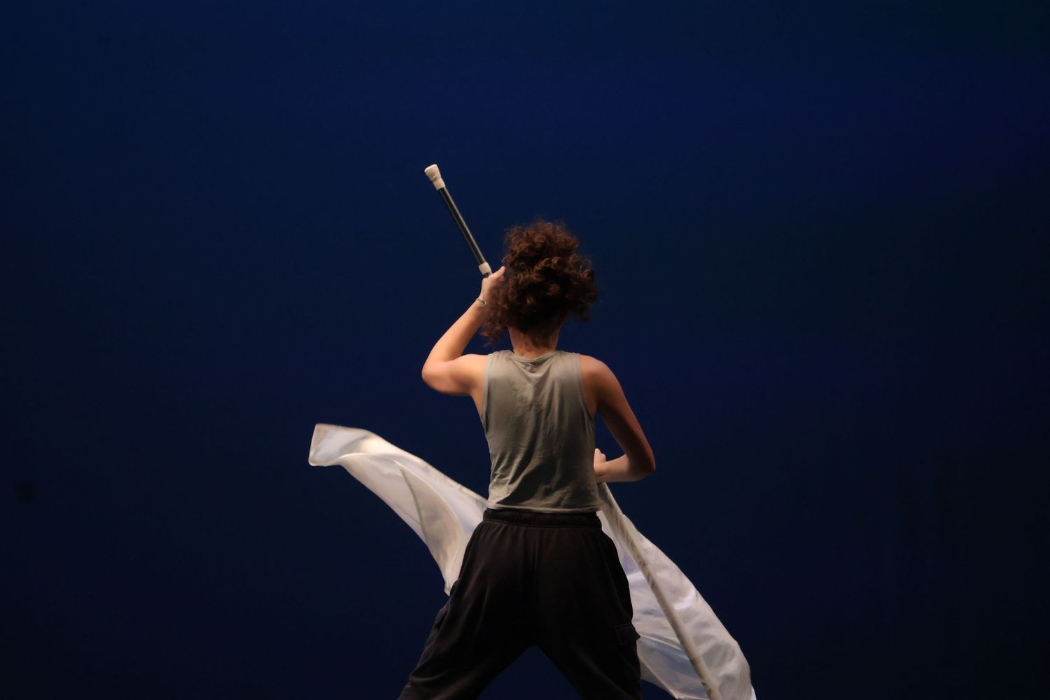 Dancer performs with flowing white fabric against dark blue background in dramatic pose.