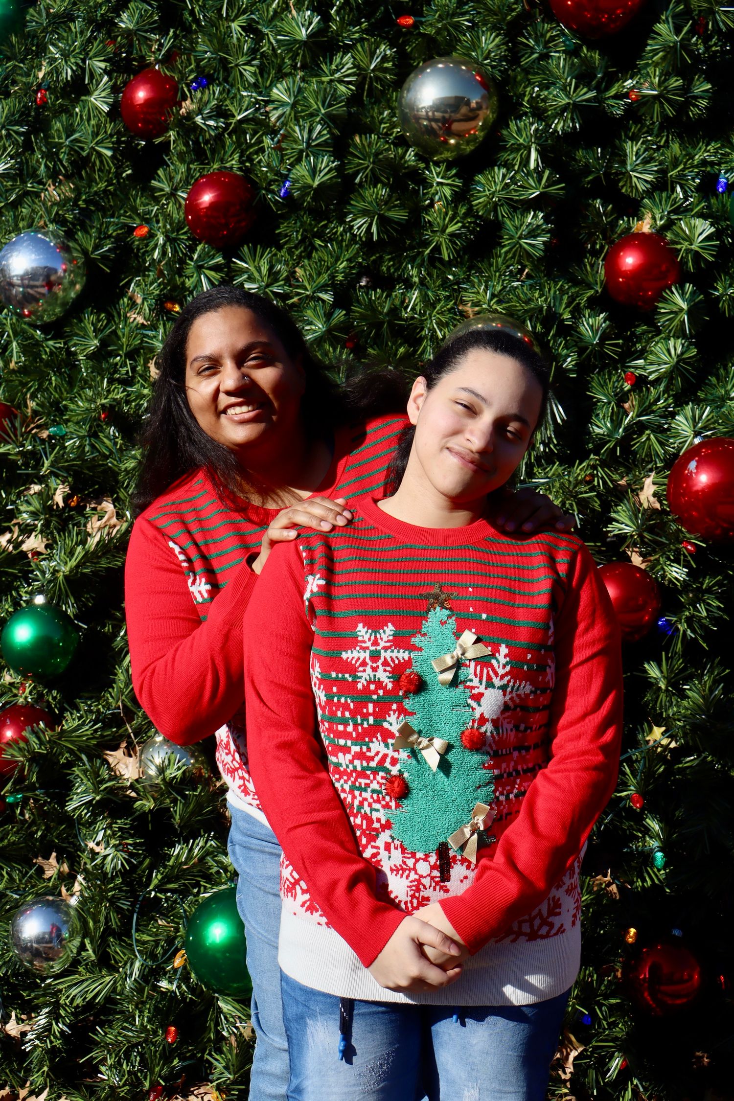 Friends in festive red sweaters pose together in front of Christmas tree with ornaments.