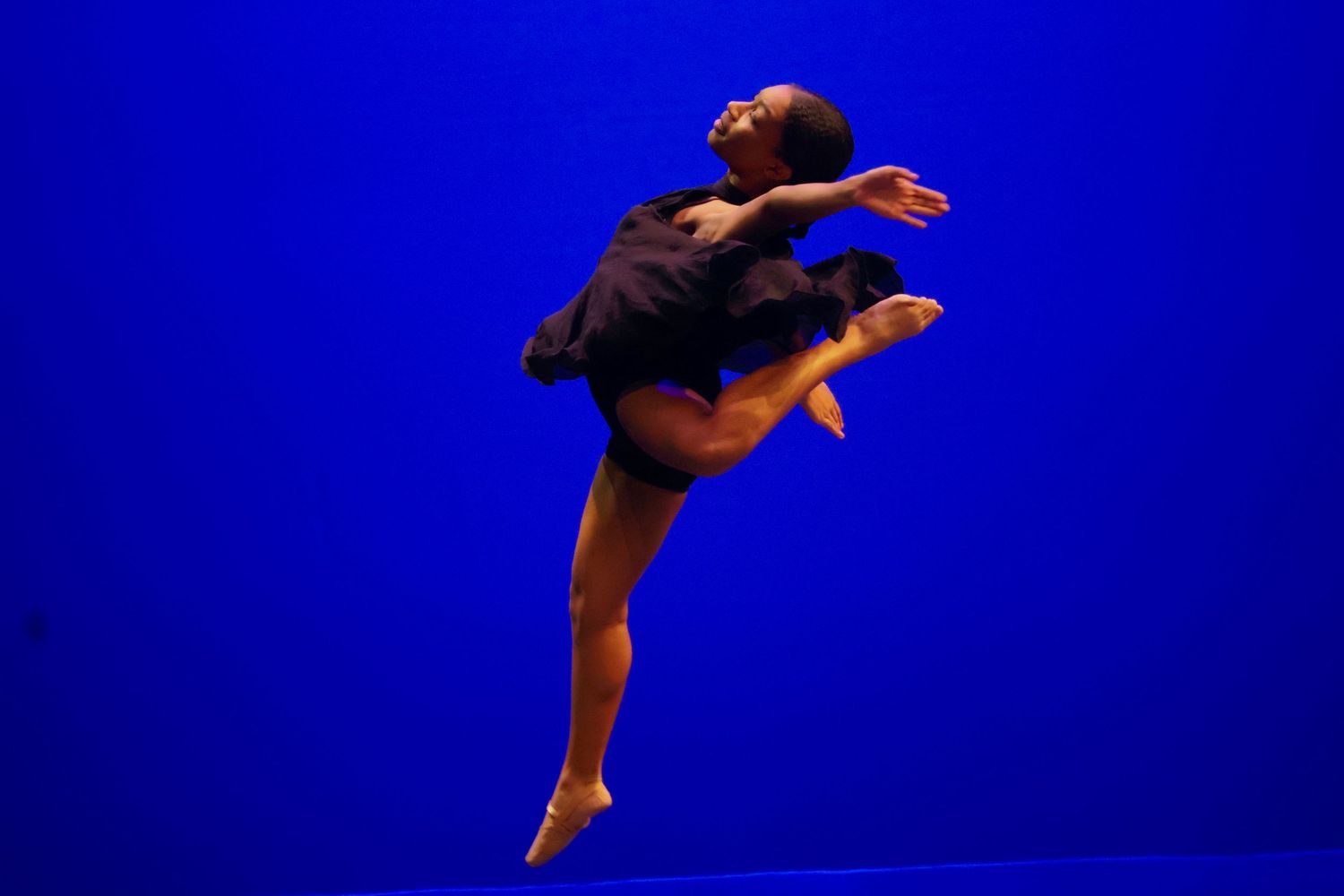 Modern dancer leaps gracefully against deep blue background in artistic performance.