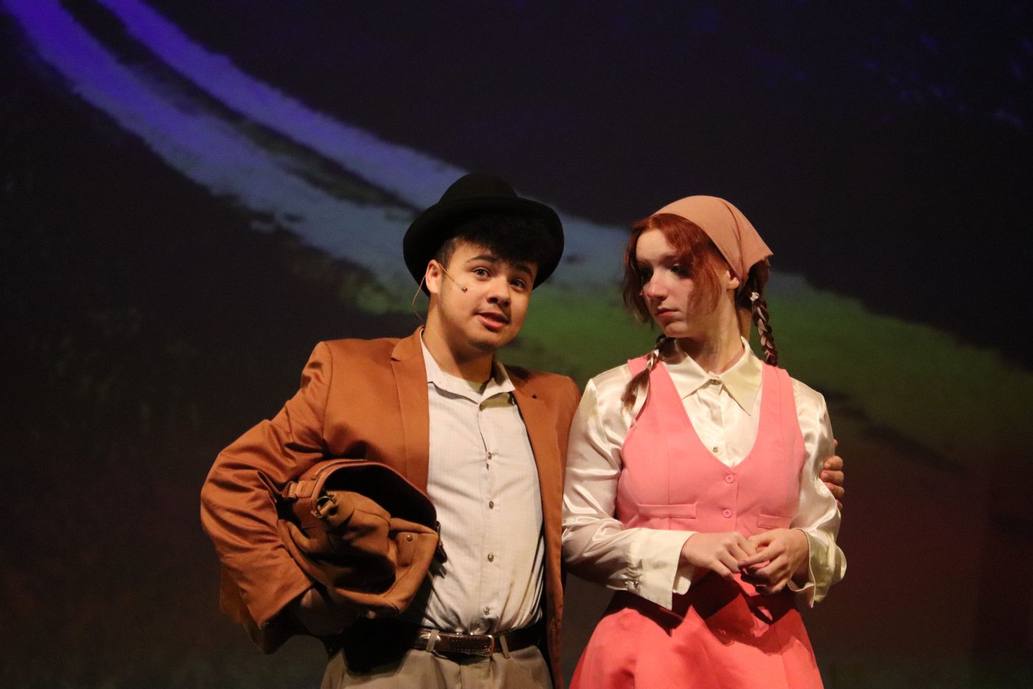 Theater performers in period costumes acting on a dimly lit stage with dramatic lighting.