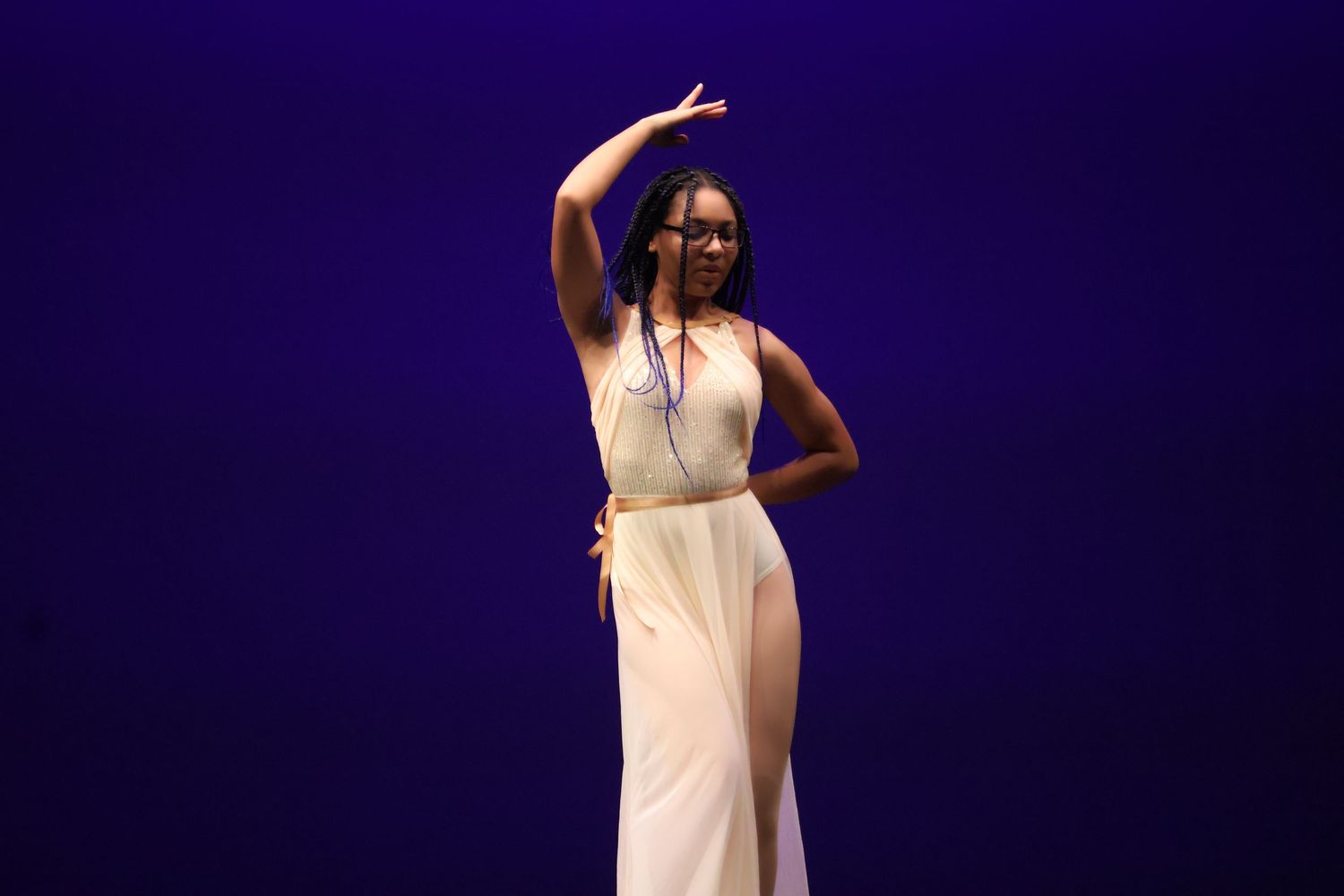 Elegant dancer in white dress performs graceful pose against purple backdrop.