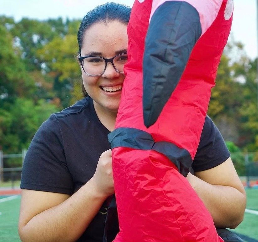 Person holding and displaying red puppet or plush toy outdoors.