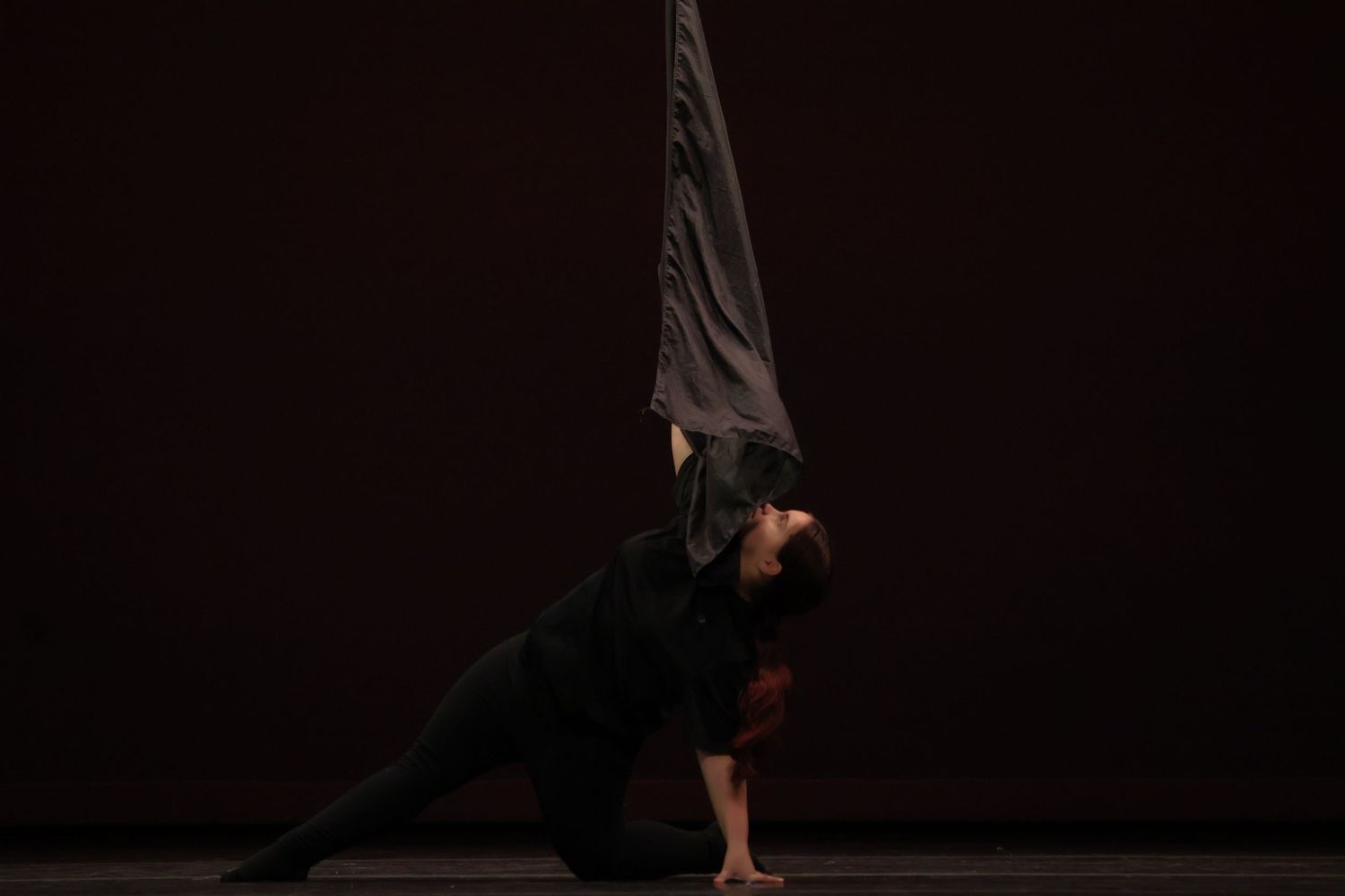 Dancers perform contemporary movements in dramatic silhouette against dark background.