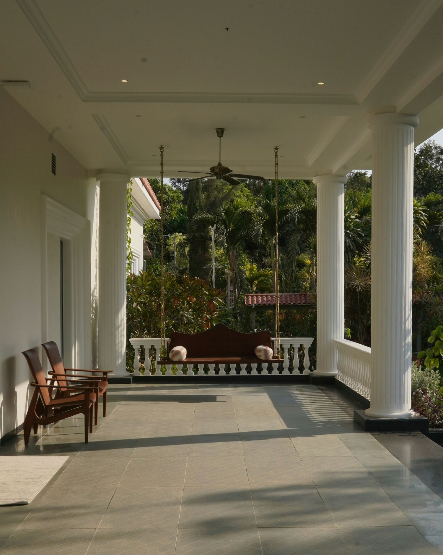 White columned pavilion with polished floors and outdoor seating area surrounded by greenery.