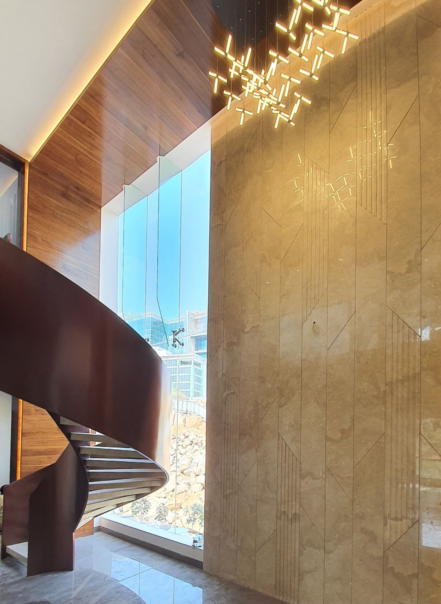 Elegant spiral staircase with wooden panels and modern lighting fixtures in a high-ceiling space.