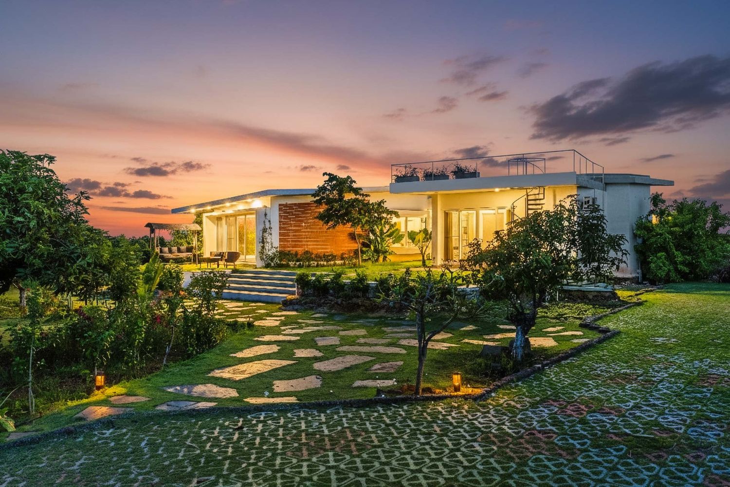 Modern luxury villa with illuminated landscaping and stone pathway at sunset.