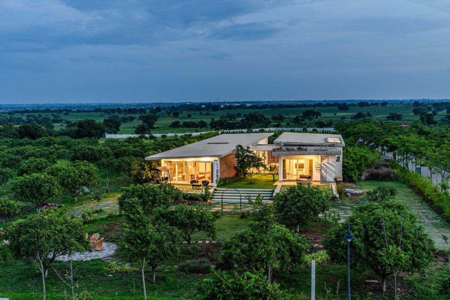 Aerial panoramic view of a modern estate surrounded by lush greenery at dusk.
