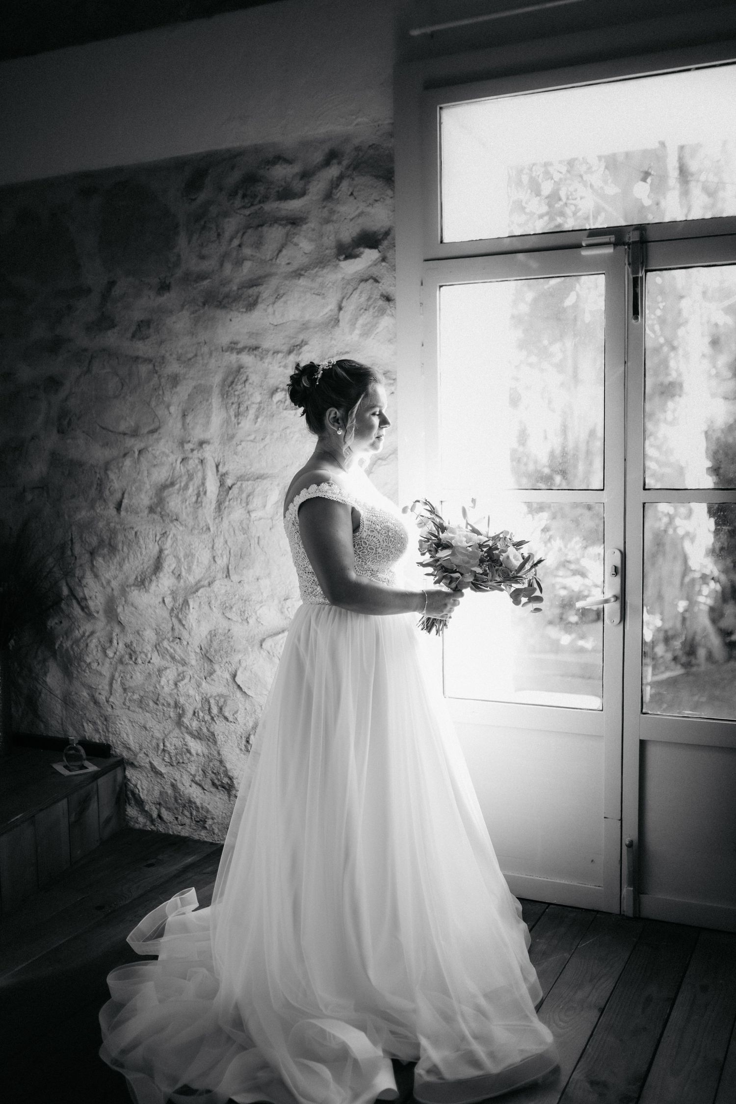 Mariée en préparation près d’une fenêtre, portrait en noir et blanc lumineux.