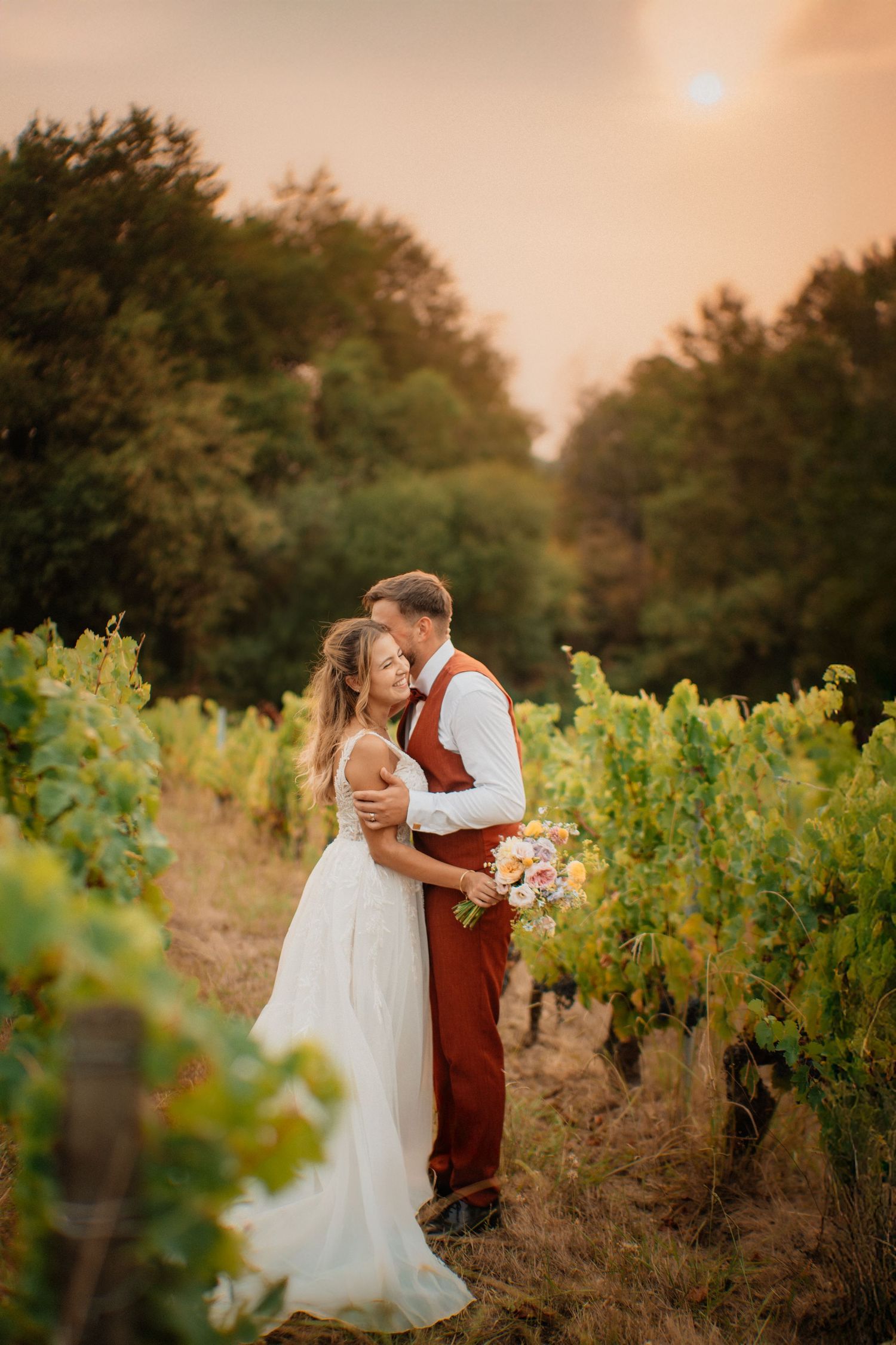 Mariés enlacés dans les vignes à la golden hour, lumière chaude et ambiance naturelle en Occitanie.