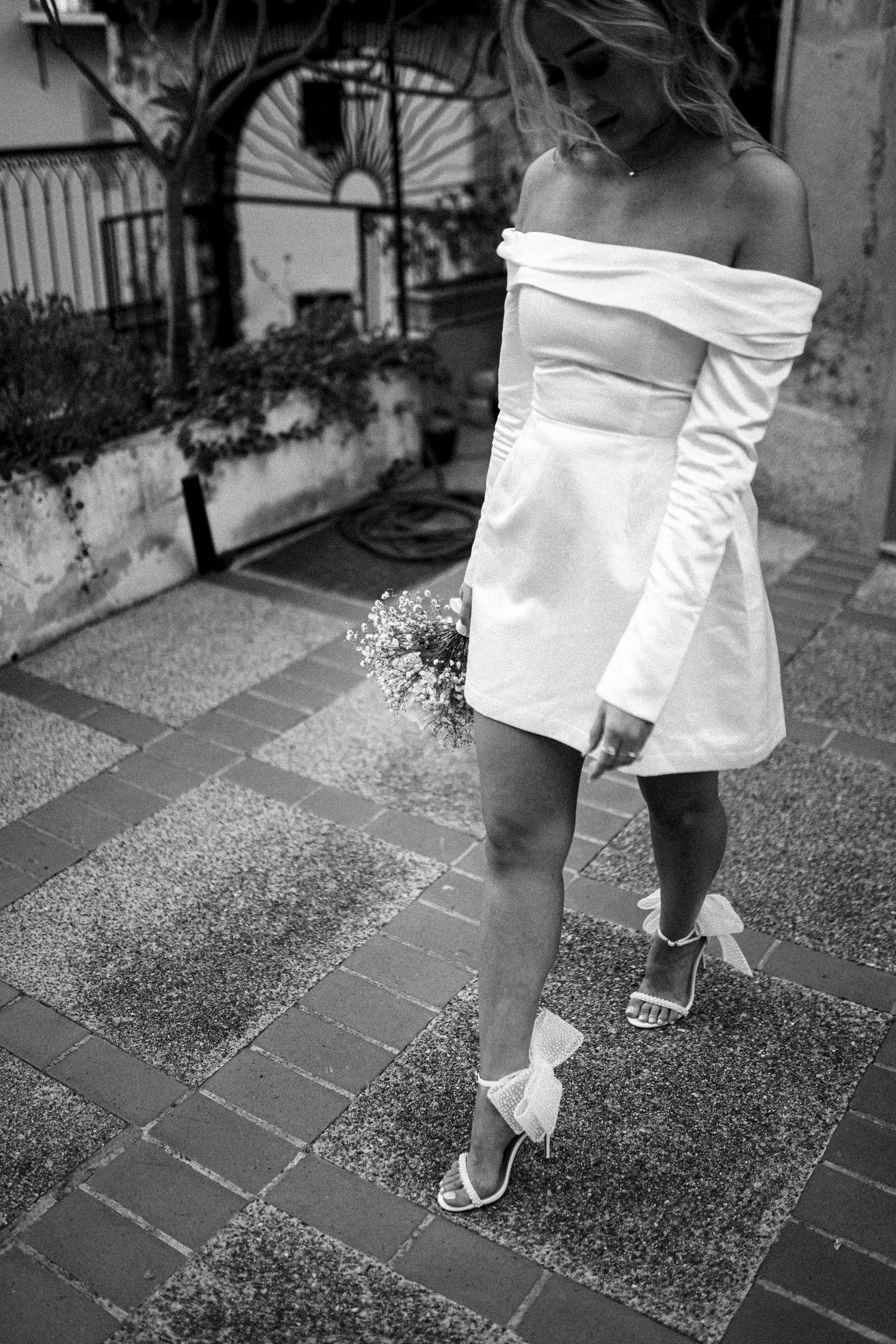 Mariée en robe courte marchant dans une cour, photo de mariage en noir et blanc à Montpellier