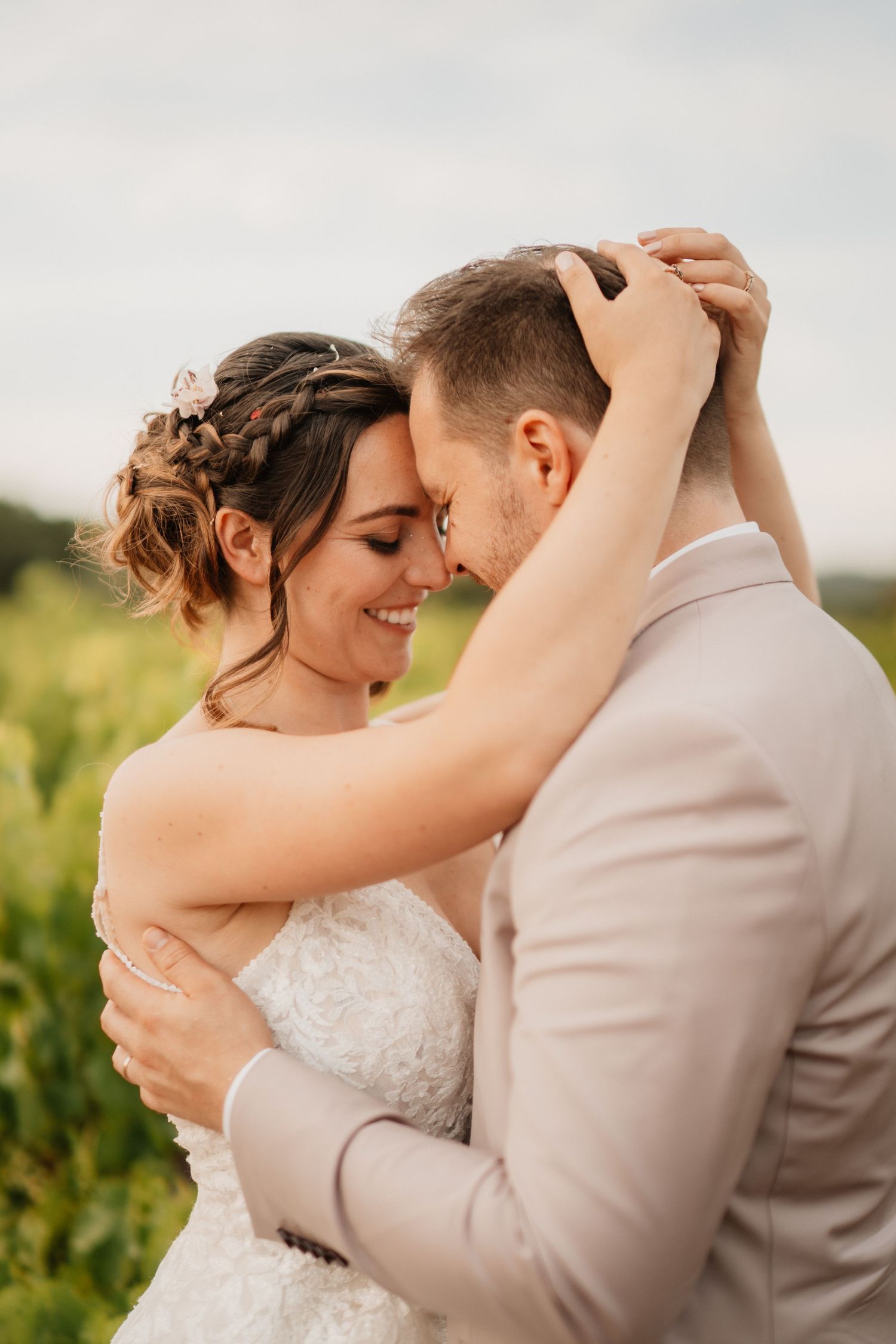 Couple de mariés enlacés dans les vignes, front contre front, lumière douce et naturelle en Occitanie.