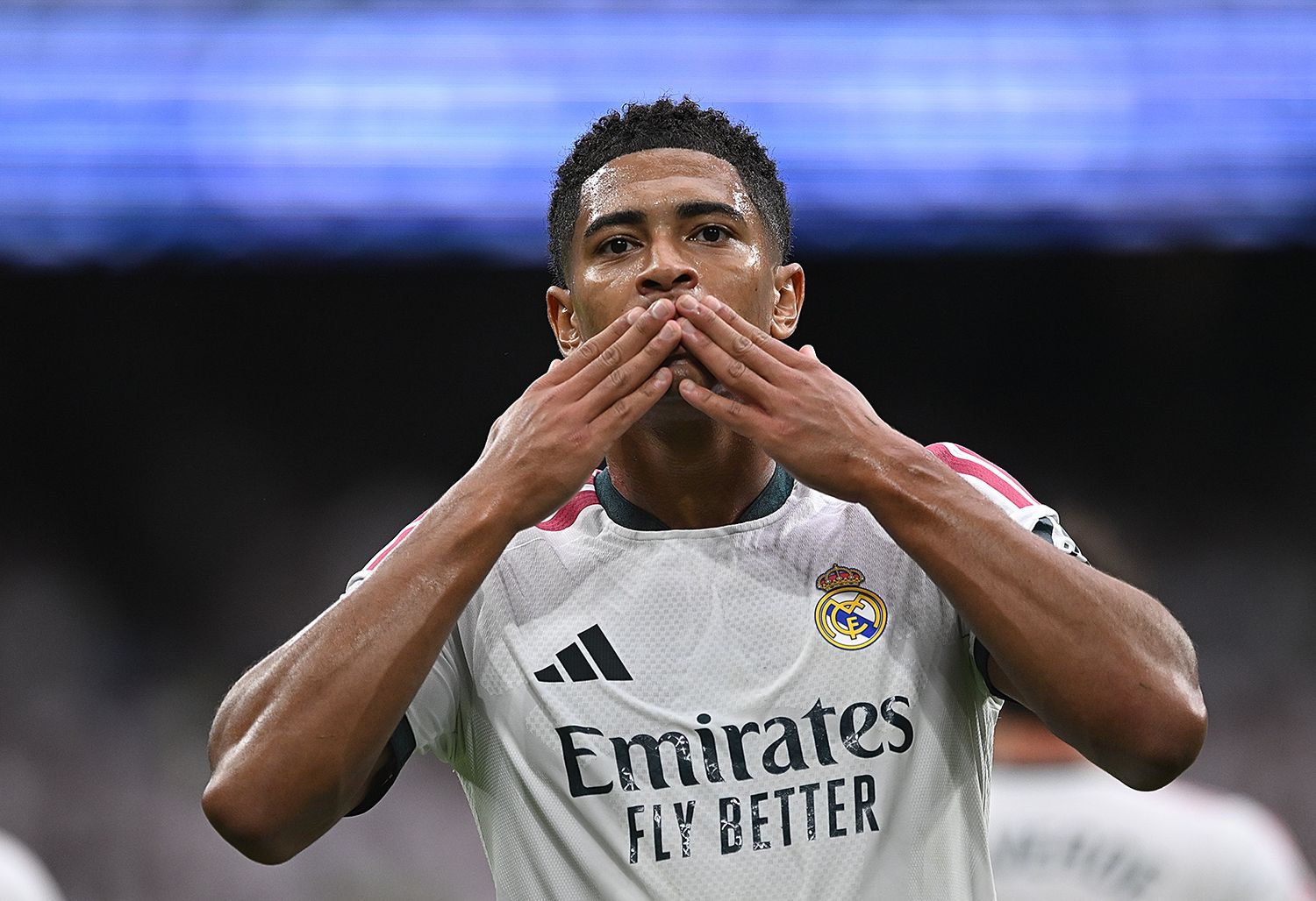 Real Madrid footballer in white Emirates jersey celebrates by blowing a kiss to fans during a match.