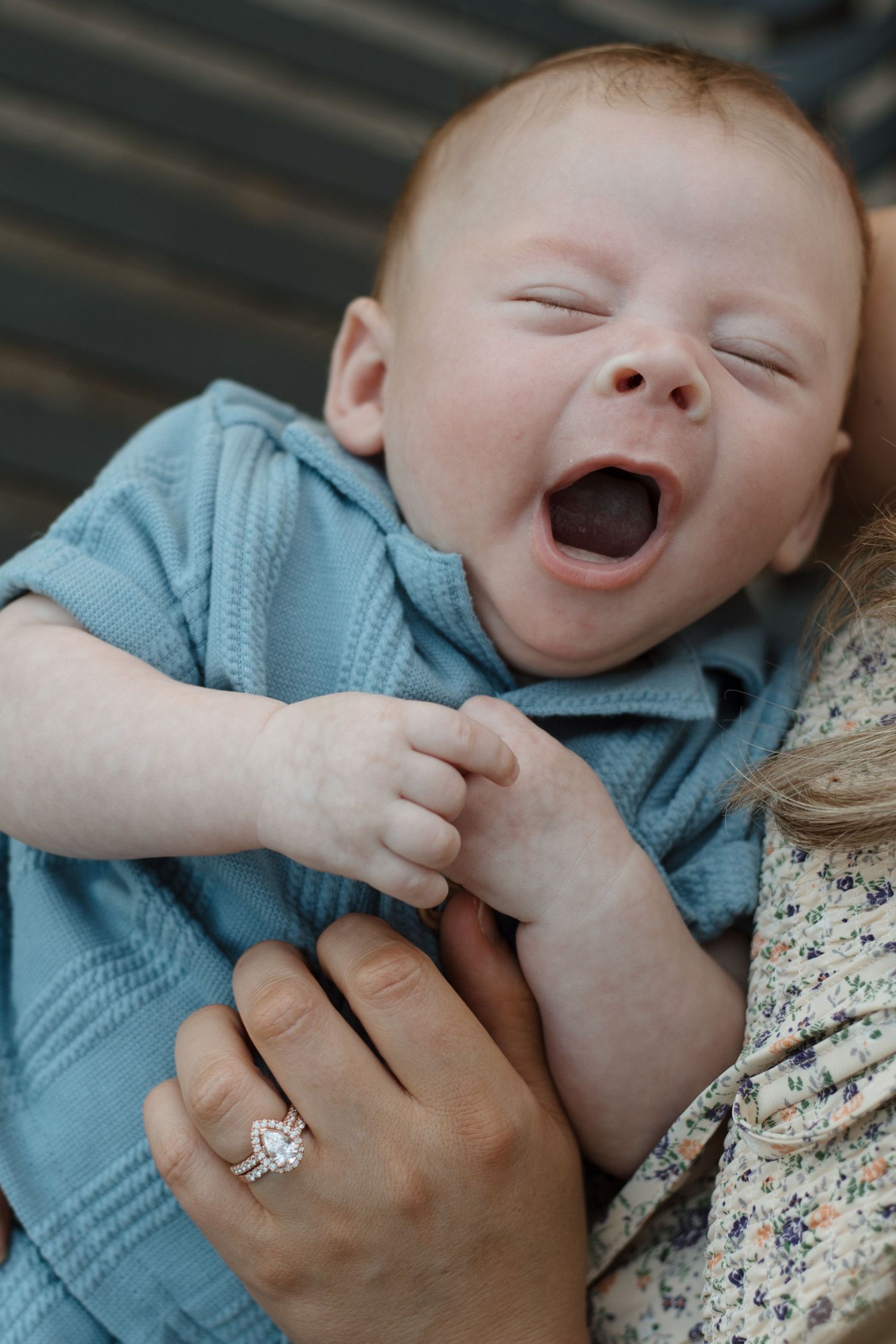 Newborn baby yawning while being held by mother wearing a diamond engagement ring.