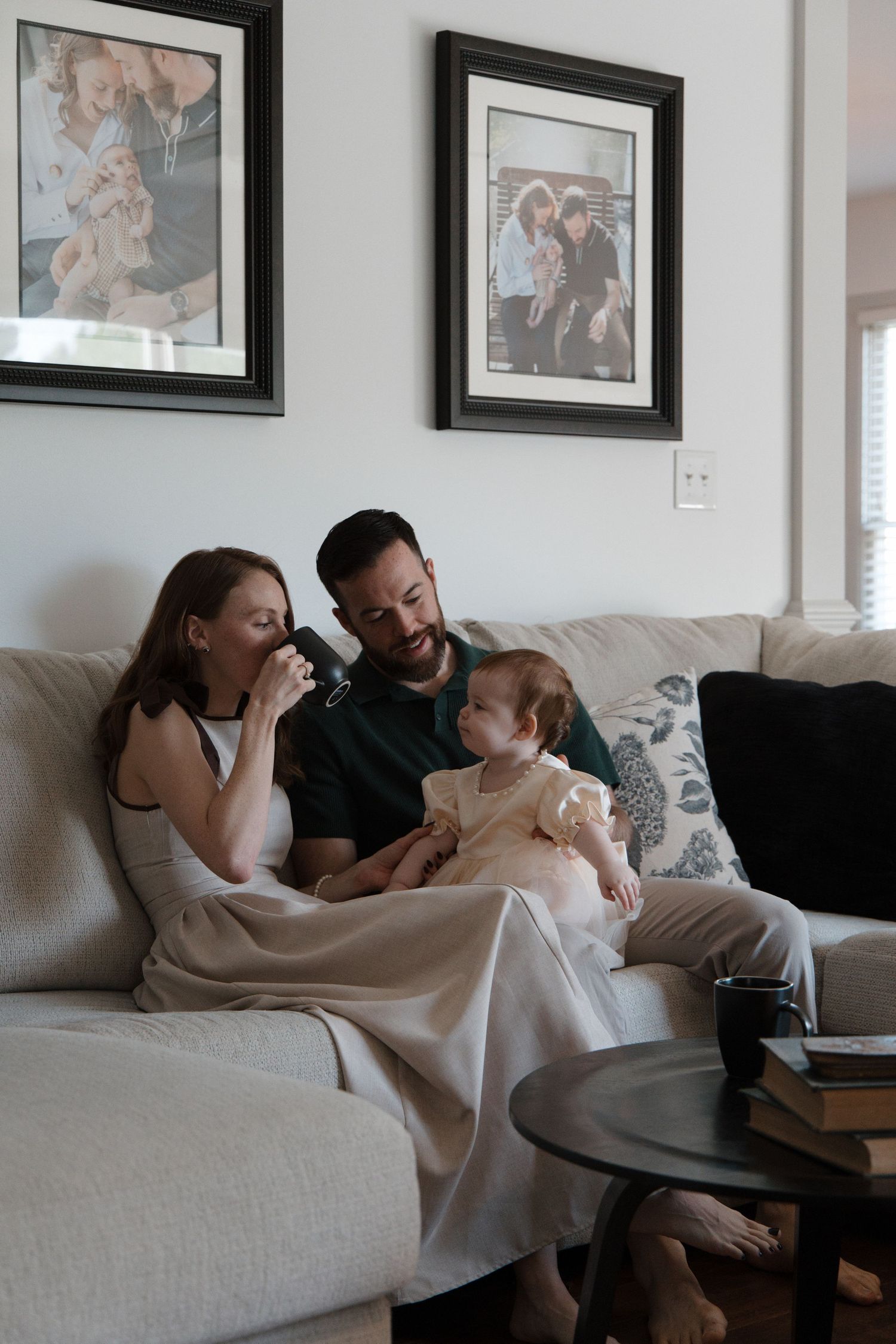 A happy family of three sits on a cozy sofa, with framed photos on the wall behind them.