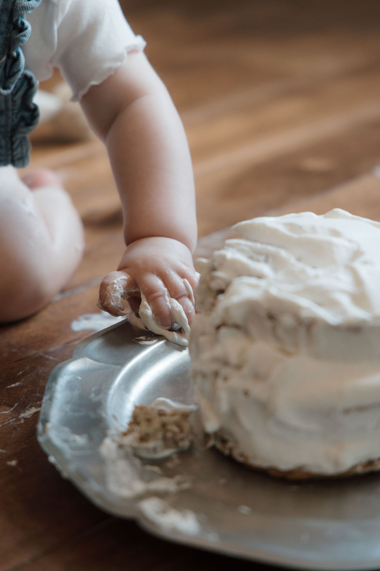 Baby smashing white frosted cake on silver platter during first birthday cake smash photo session.