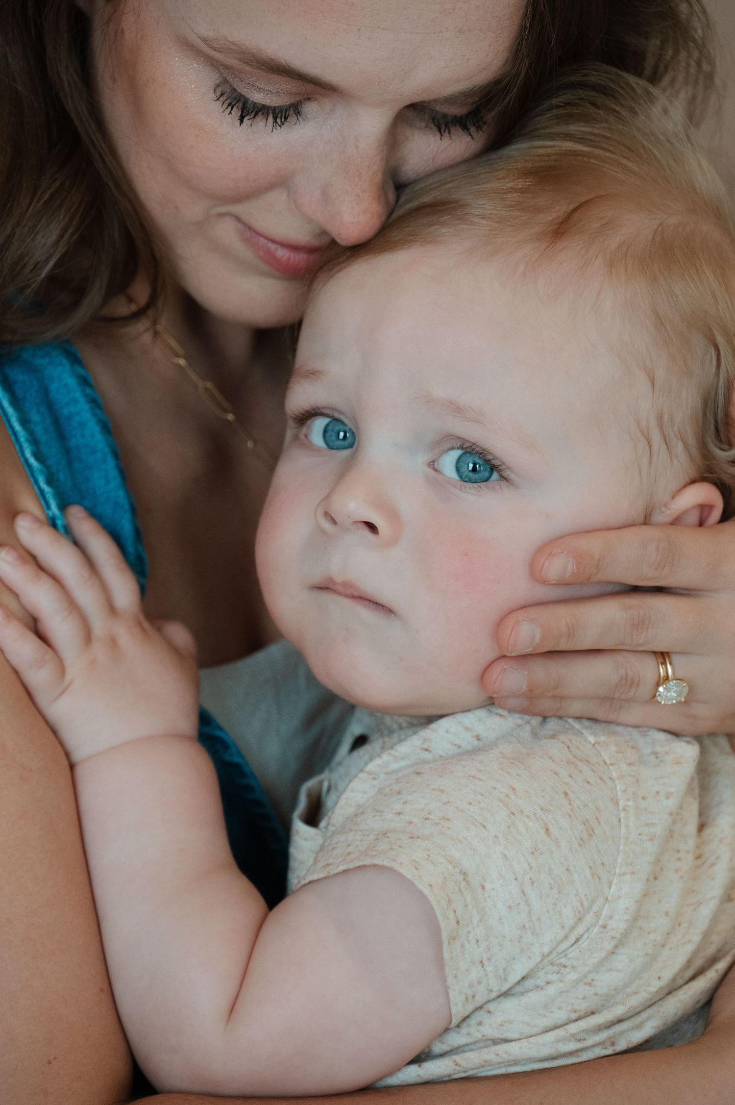 A mother tenderly holds her blue-eyed baby close, gently cradling the child's face while wearing a gold ring. CHARLOTTE NC