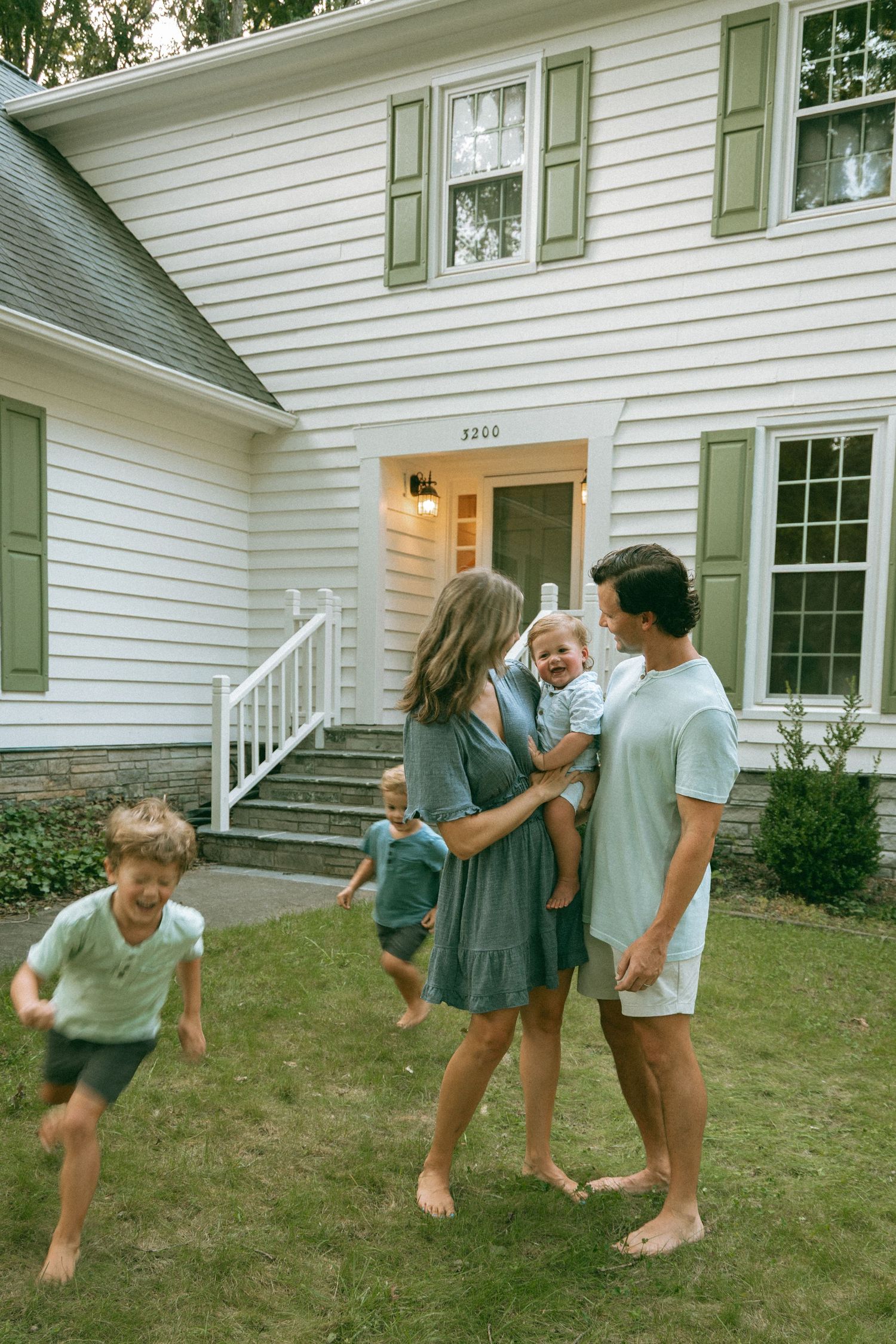 Happy family with children playing outside their white house with green shutters on a summer day.