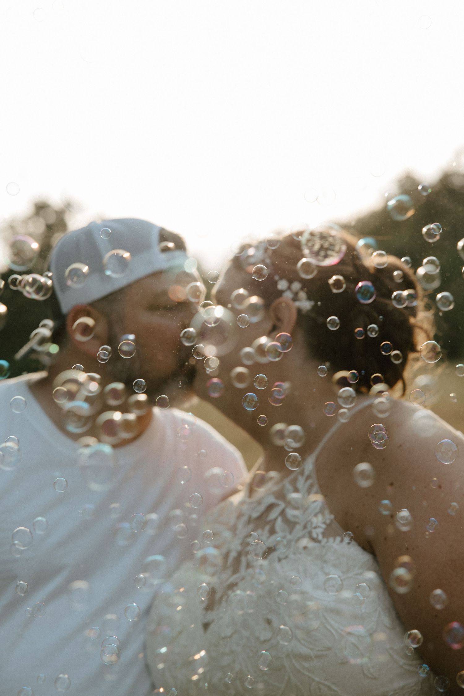 A couple shares a romantic kiss surrounded by floating bubbles during their outdoor wedding ceremony.