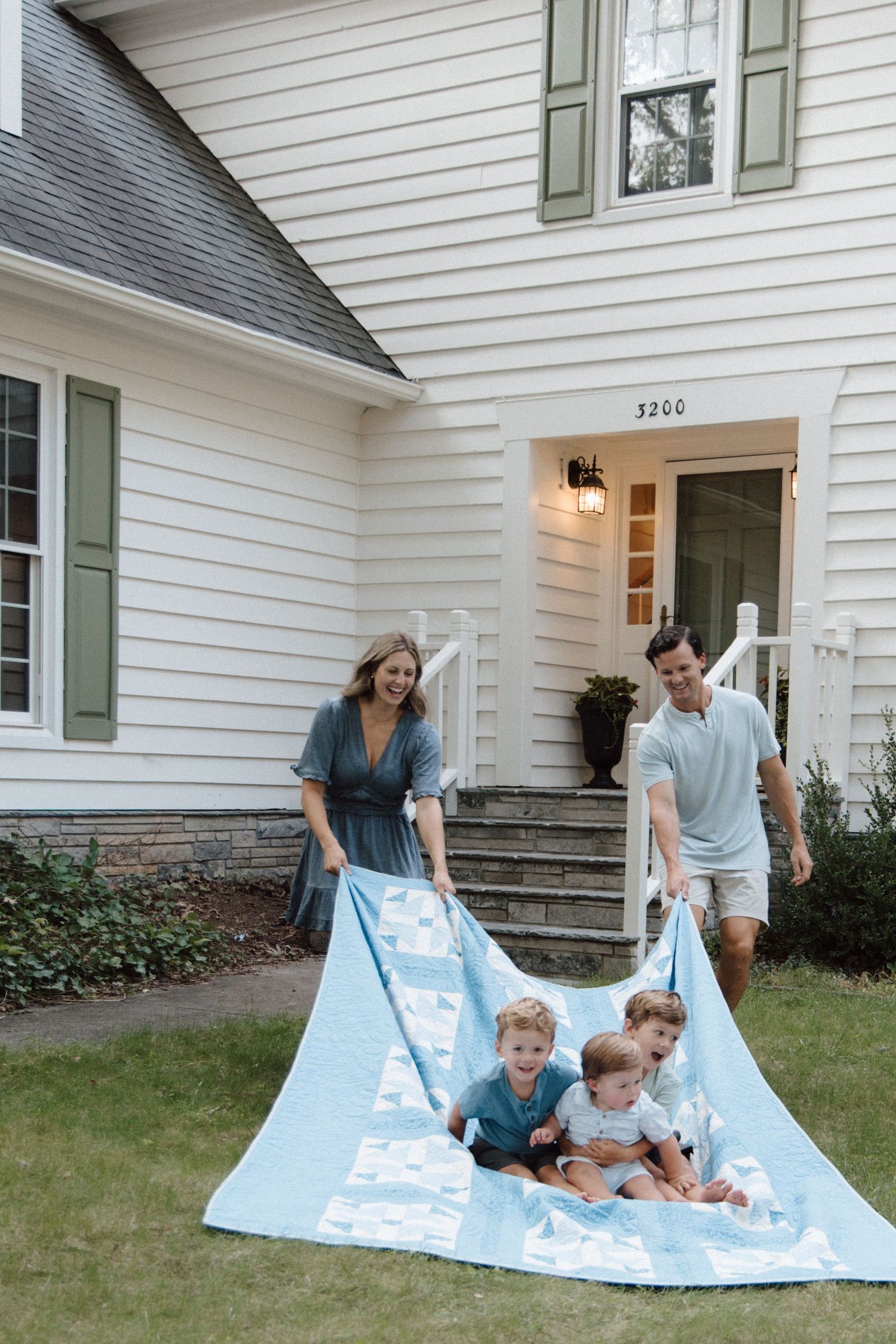 Family of four playing with a light blue blanket on the front lawn of a white colonial home at 3200.