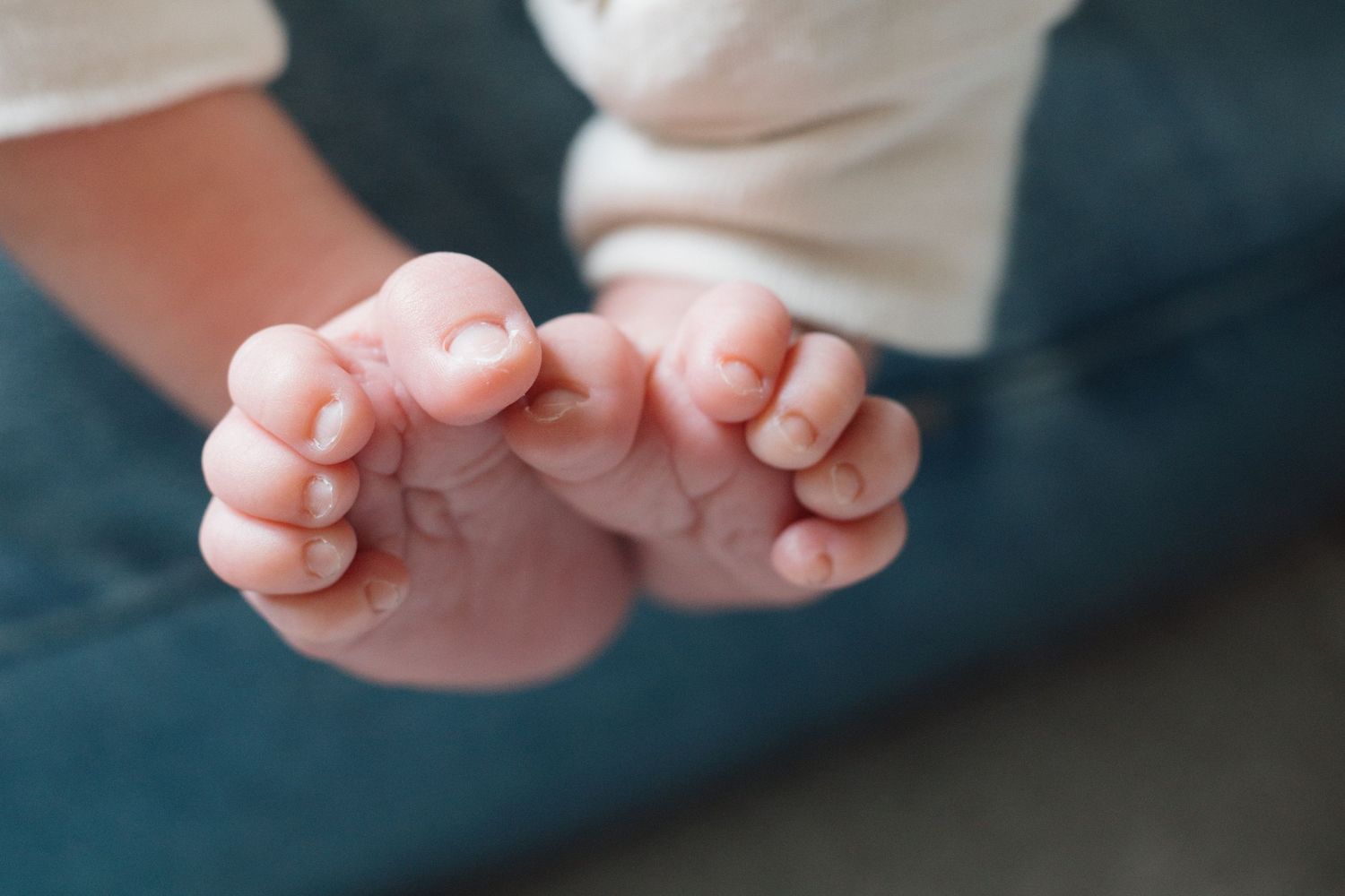 Close-up of newborn baby tiny feet and toes resting on a teal surface.