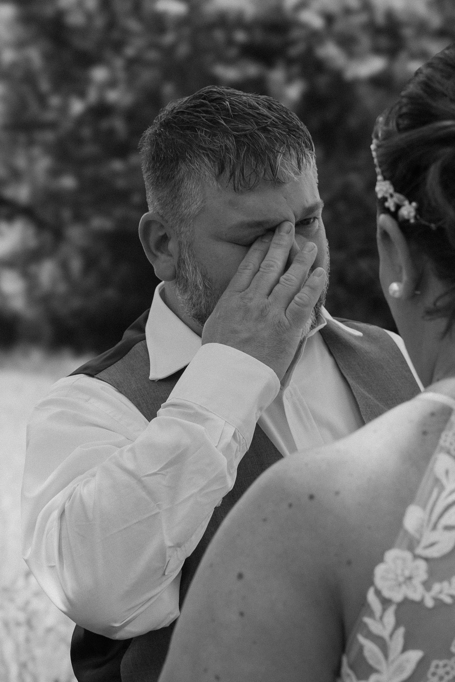 Emotional groom wiping tears during wedding ceremony in black and white photo.