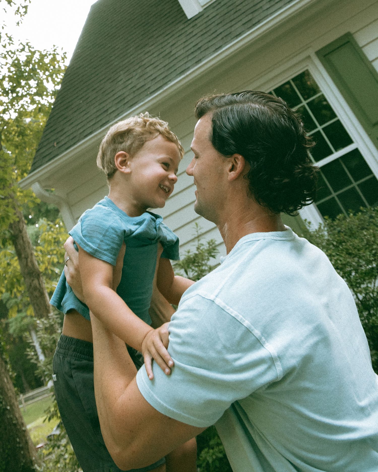 Loving father lifting and smiling at his young son outside their home.