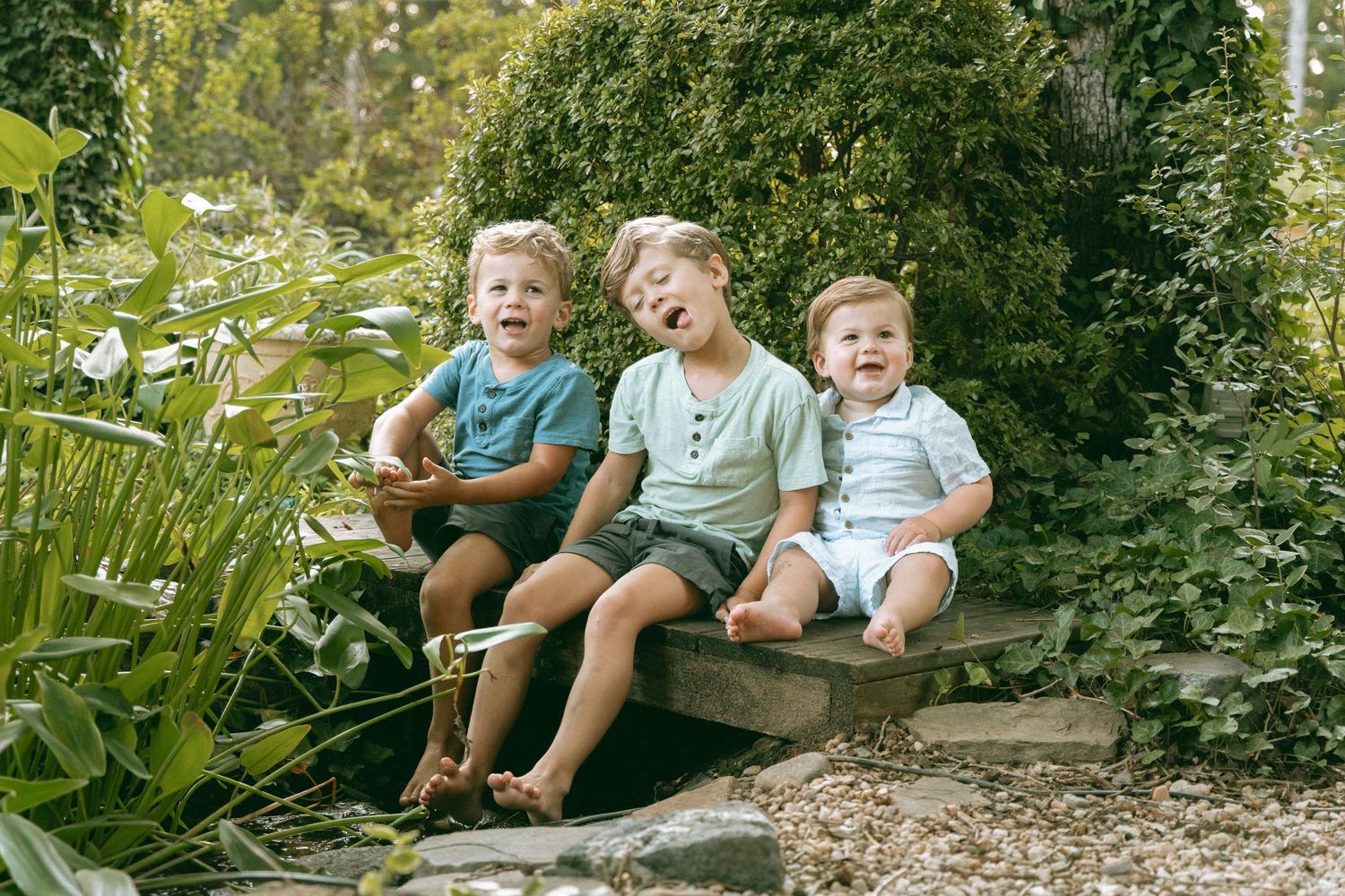 Three happy young brothers sitting together laughing on a garden bench outdoors.