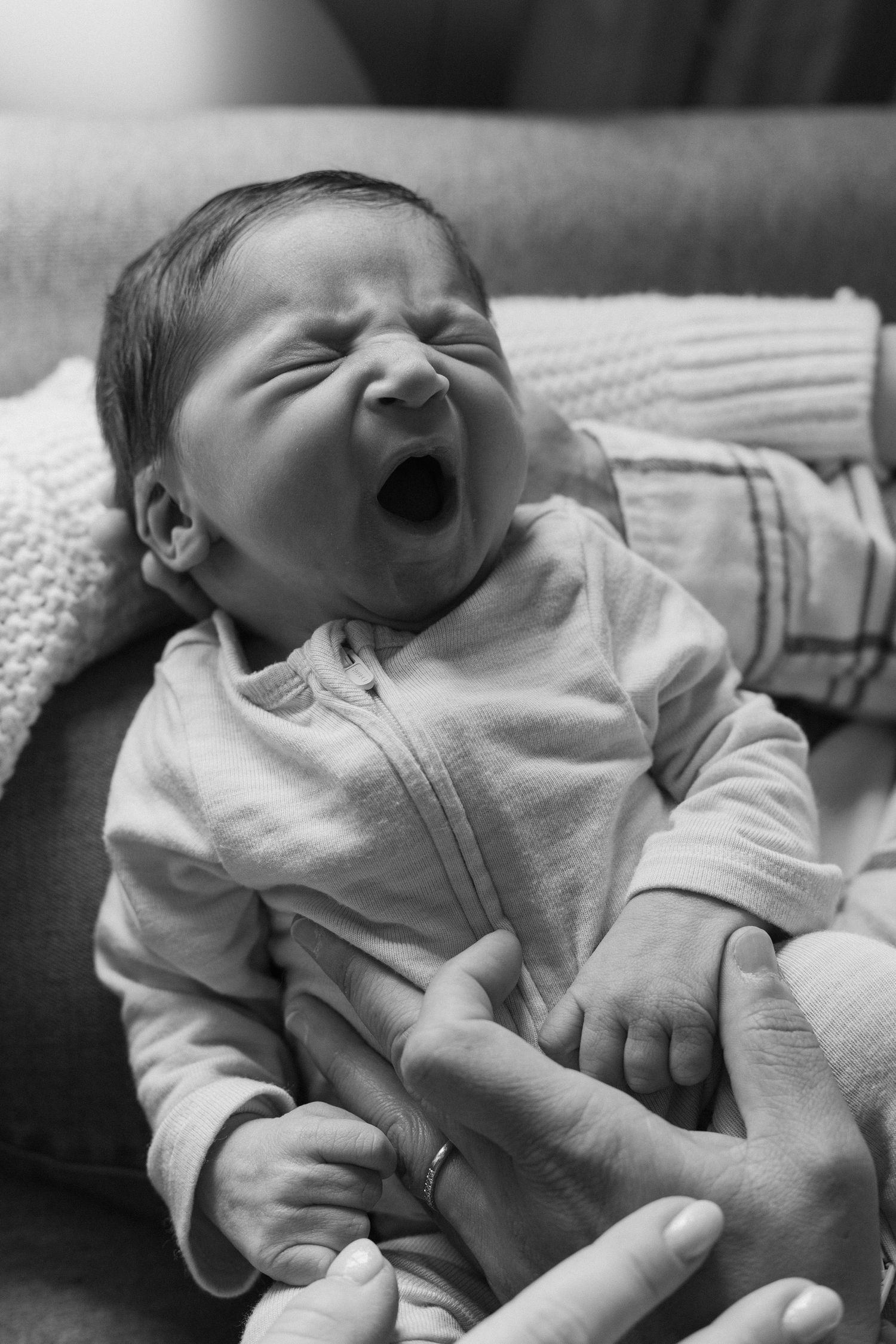 Black and white photo of a newborn baby yawning while being held by a parent's hands.