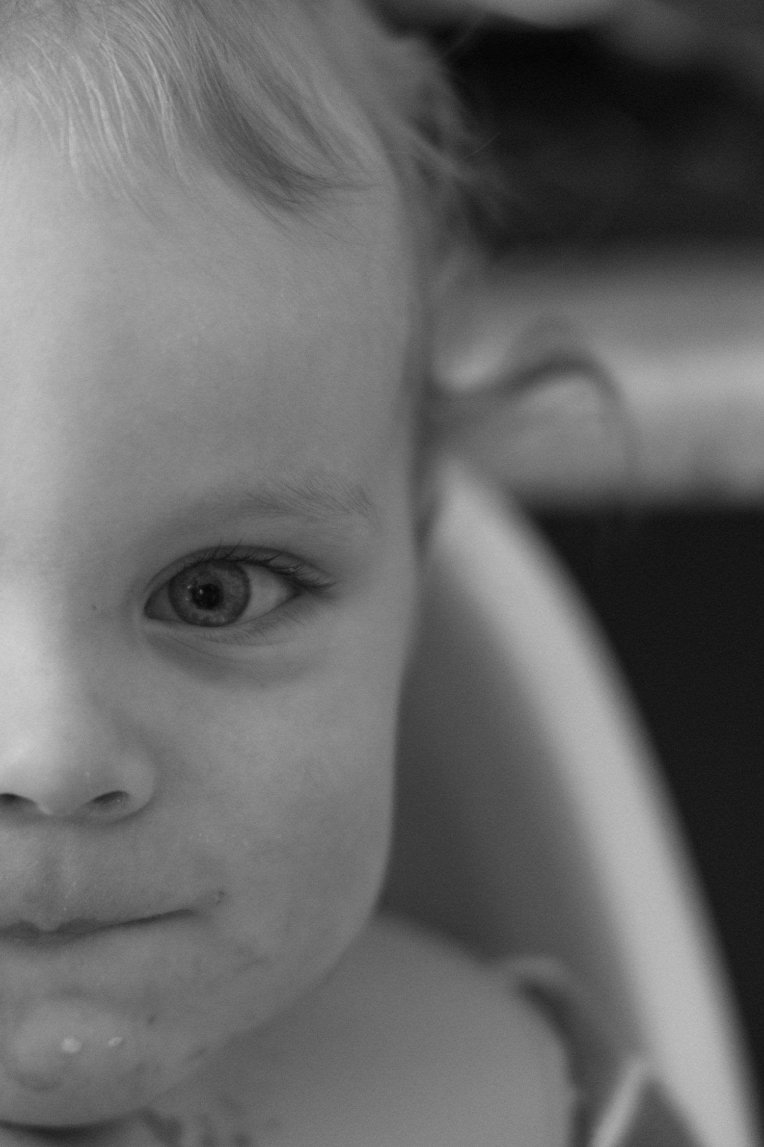 Black and white close-up portrait of a young toddler with expressive eyes and food on their chin.