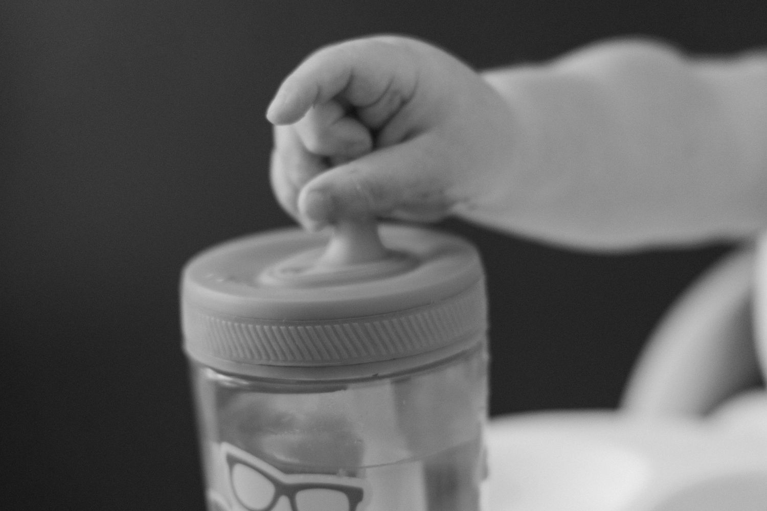 Baby hand reaching into a clear jar with glasses logo in black and white close-up photo.
