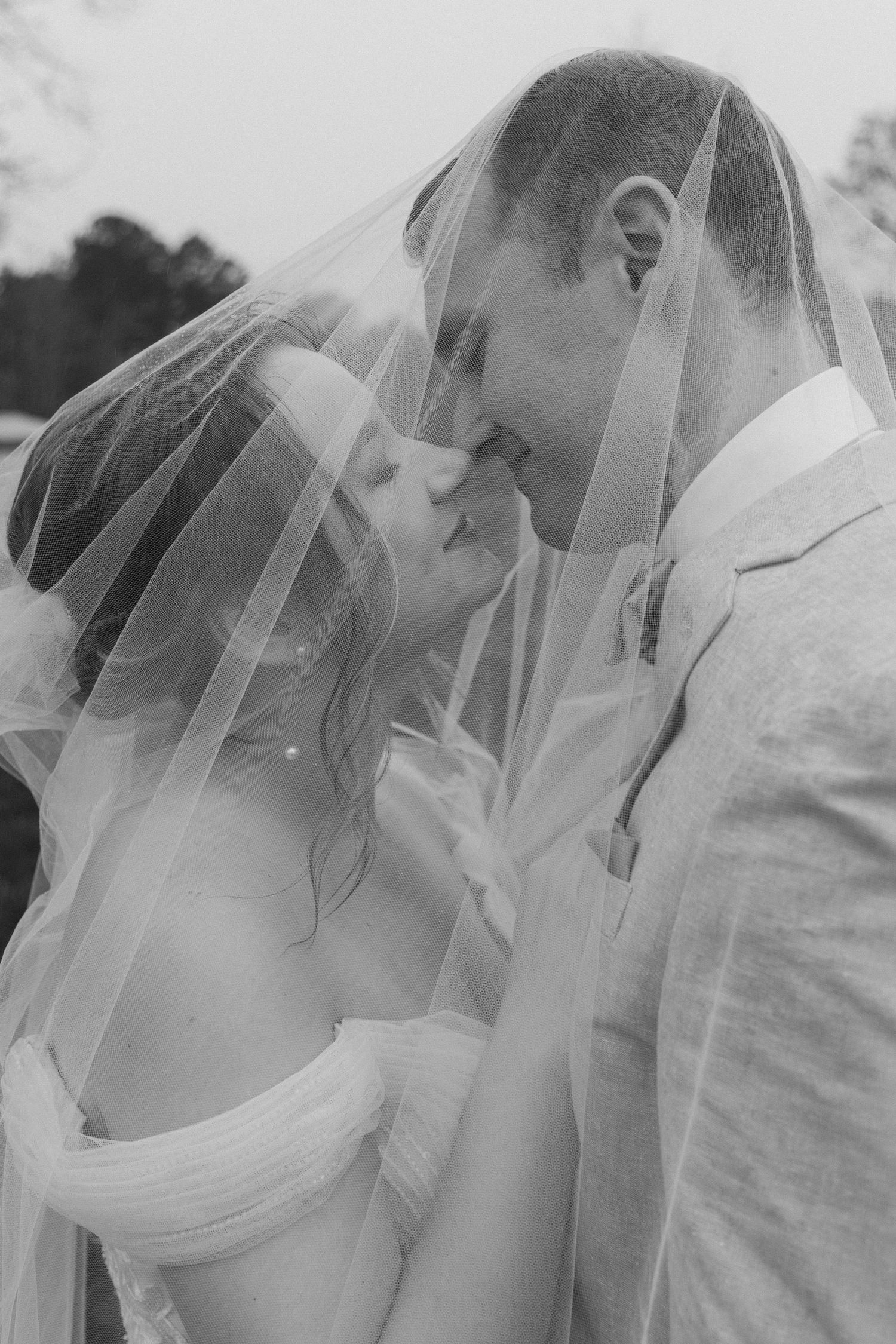 Black and white photo of bride and groom kissing under wedding veil on their wedding day. CHARLOTTE NC WEDDING PHOTOGRAPHER