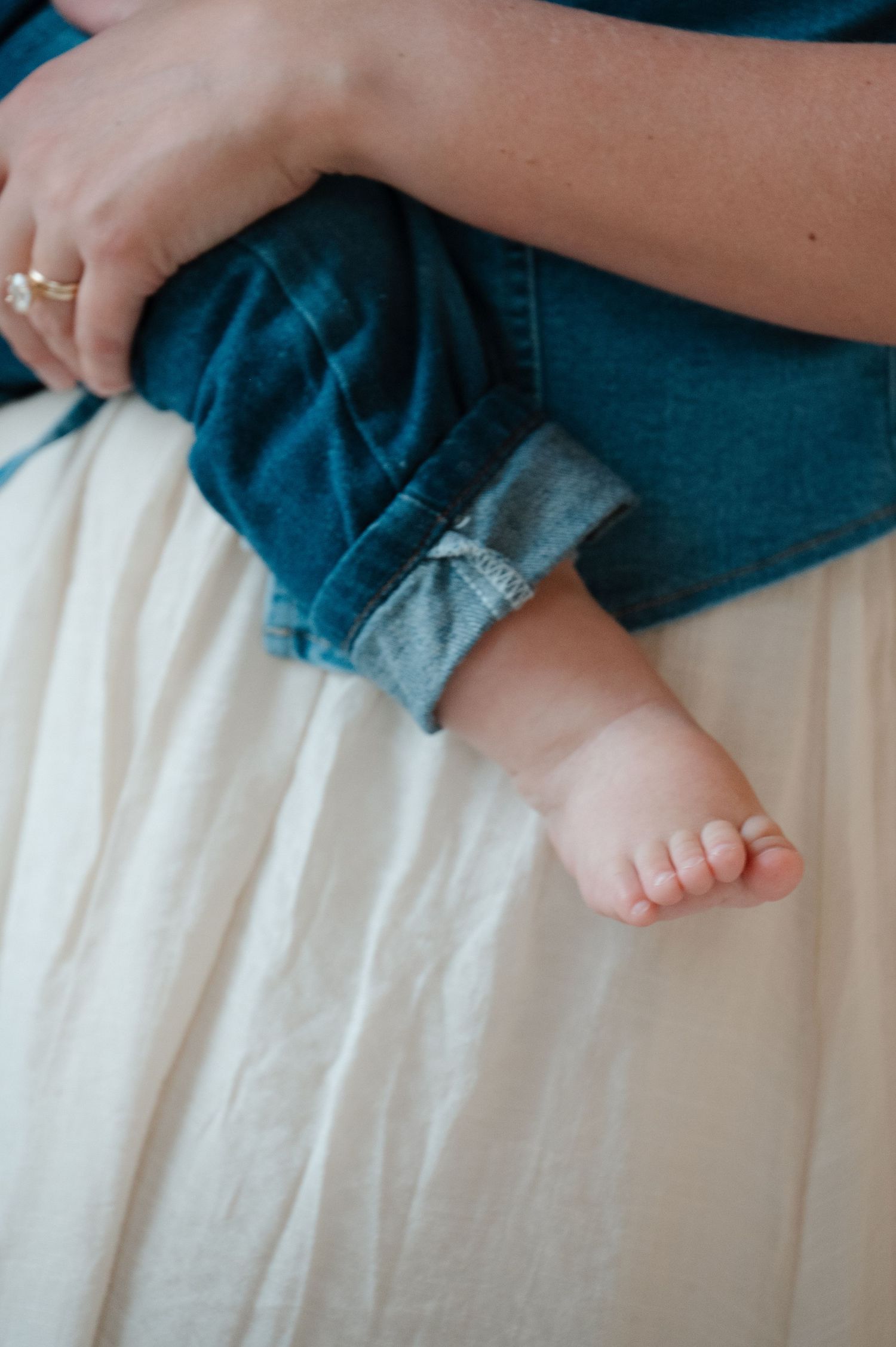 A mother holds her newborn baby dressed in tiny rolled-up denim jeans, with one small bare foot visible.