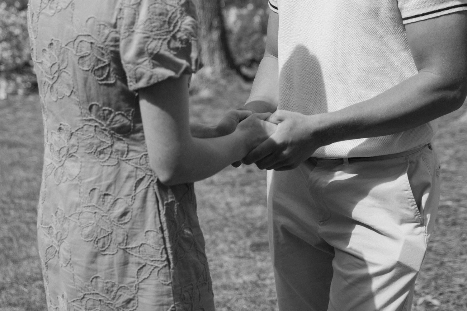 Black and white photo of a couple holding hands outdoors, sharing a romantic moment in a garden setting WITH ENGAGEMENT RING IN POCKET