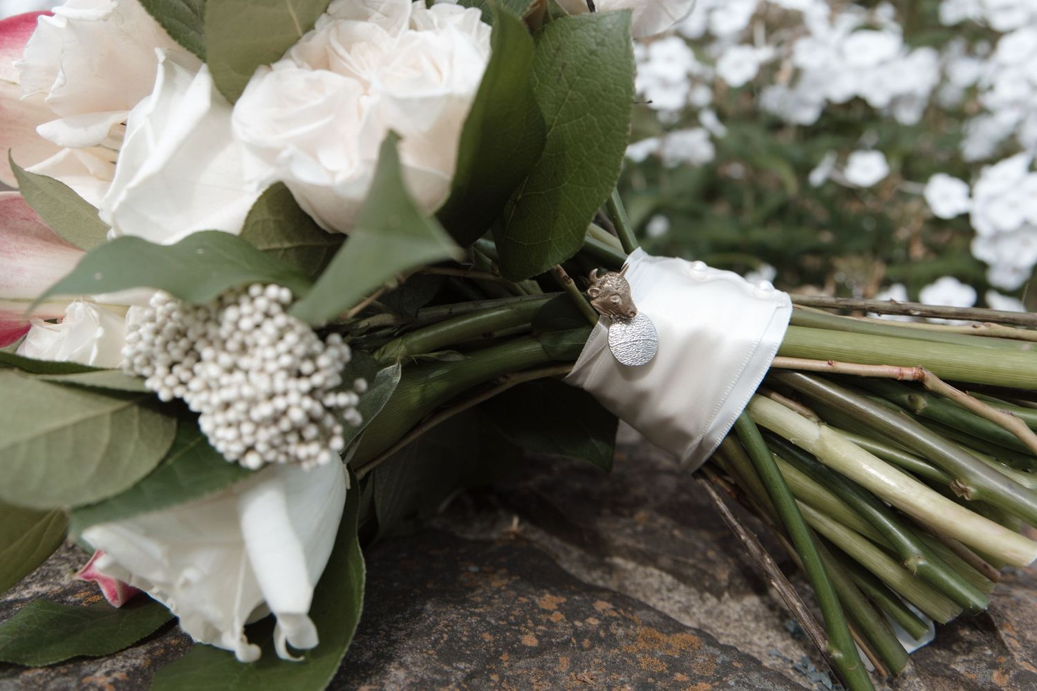White roses and greenery bridal bouquet with pearl accents and satin ribbon resting on a stone surface. CHARLOTTE NC