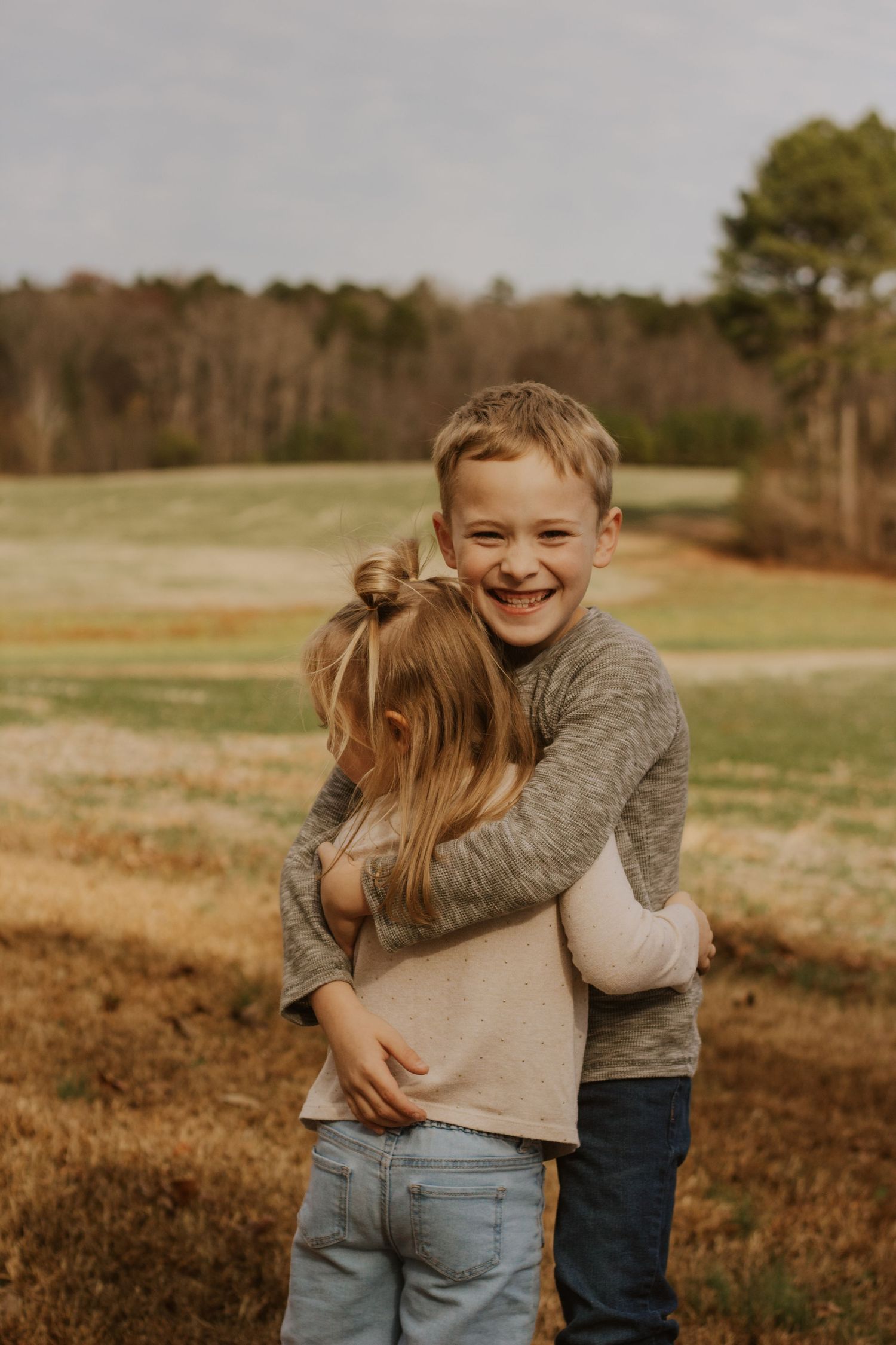 Smiling boy hugs younger girl in an autumn outdoor setting.