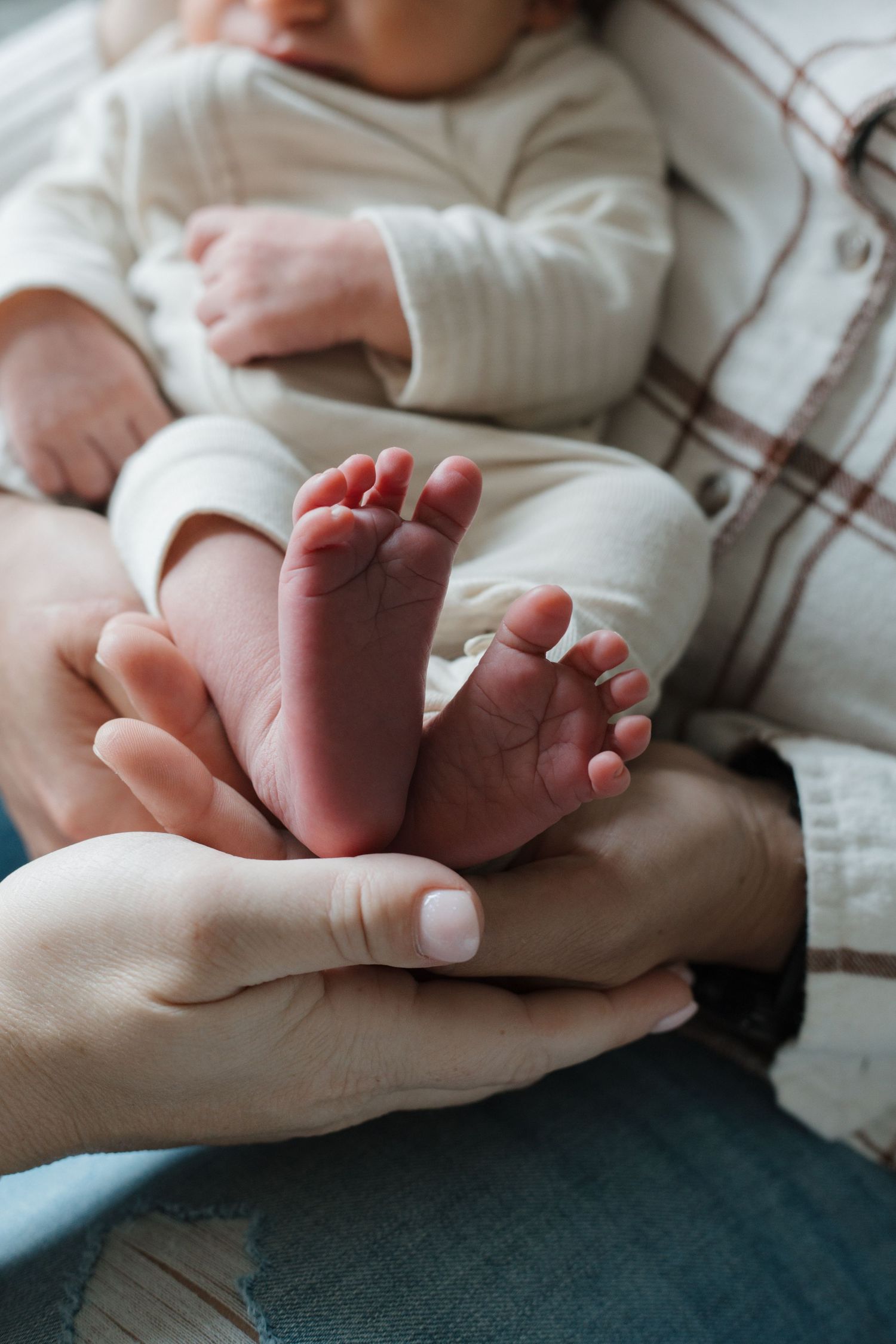 Close-up of newborn baby tiny feet cradled gently in parents hands, wearing white onesie.