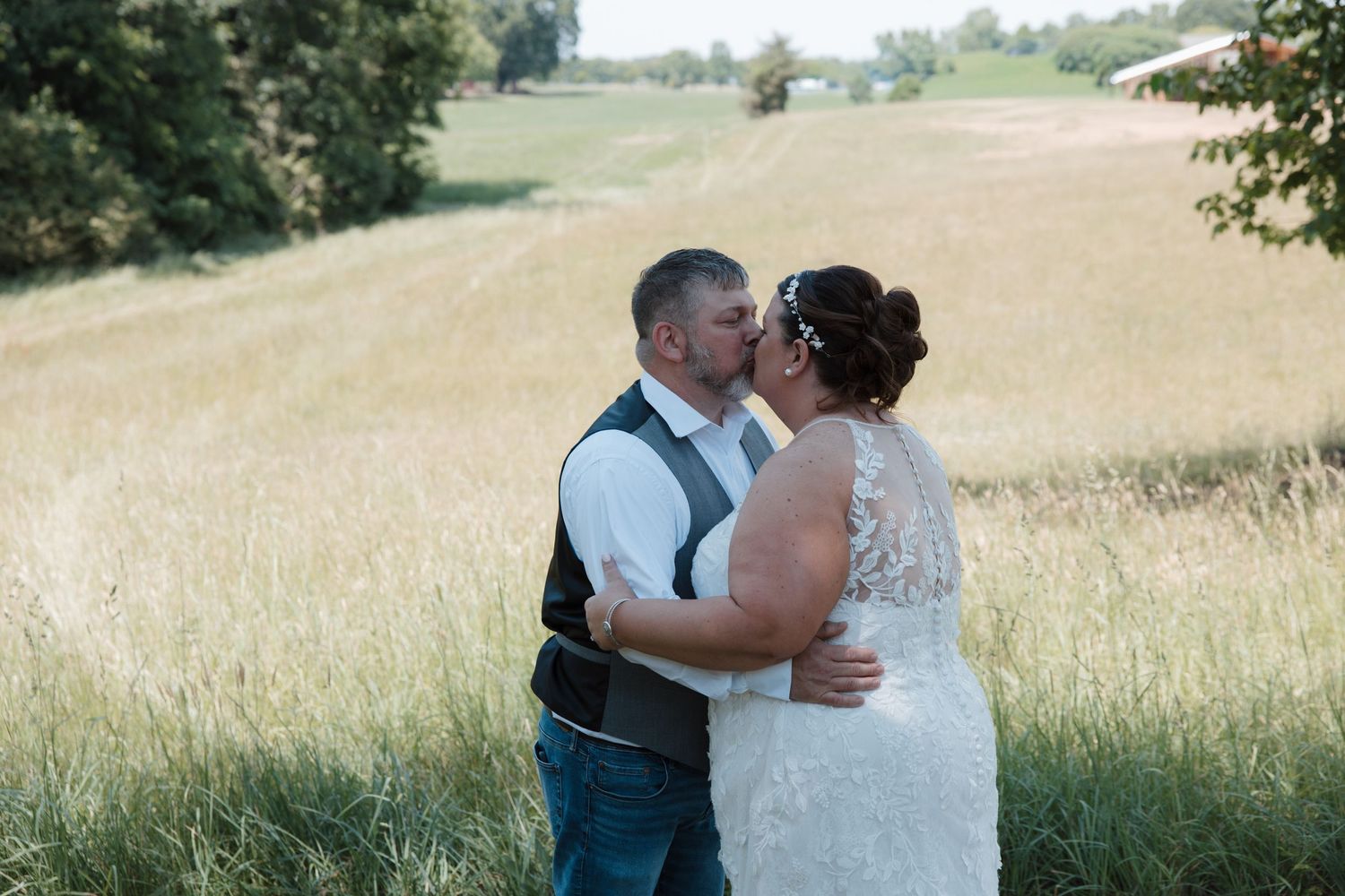Bride and groom share a romantic kiss in a golden field on their wedding day.