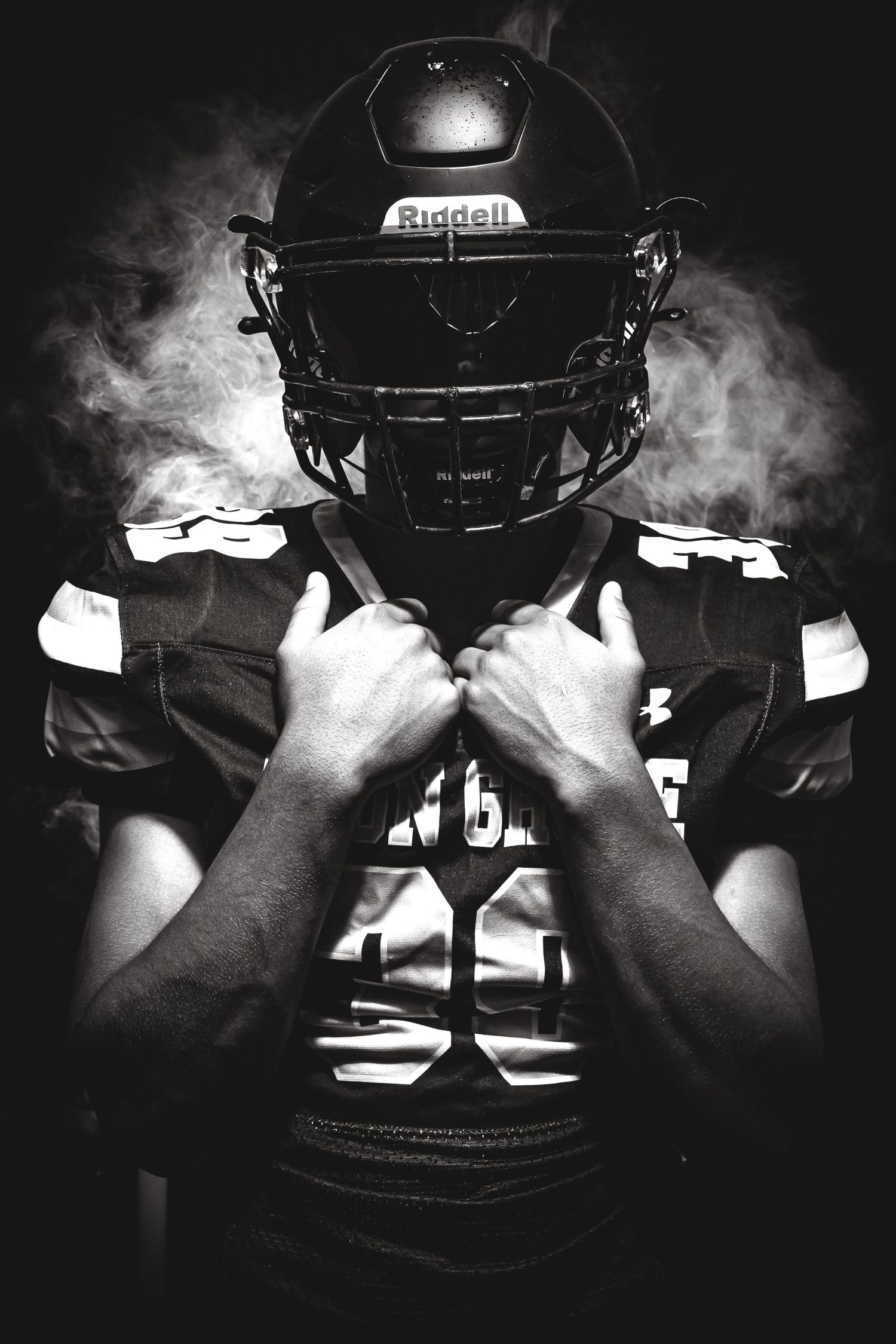 Dramatic black and white photo of football player in Riddell helmet surrounded by smoke.
