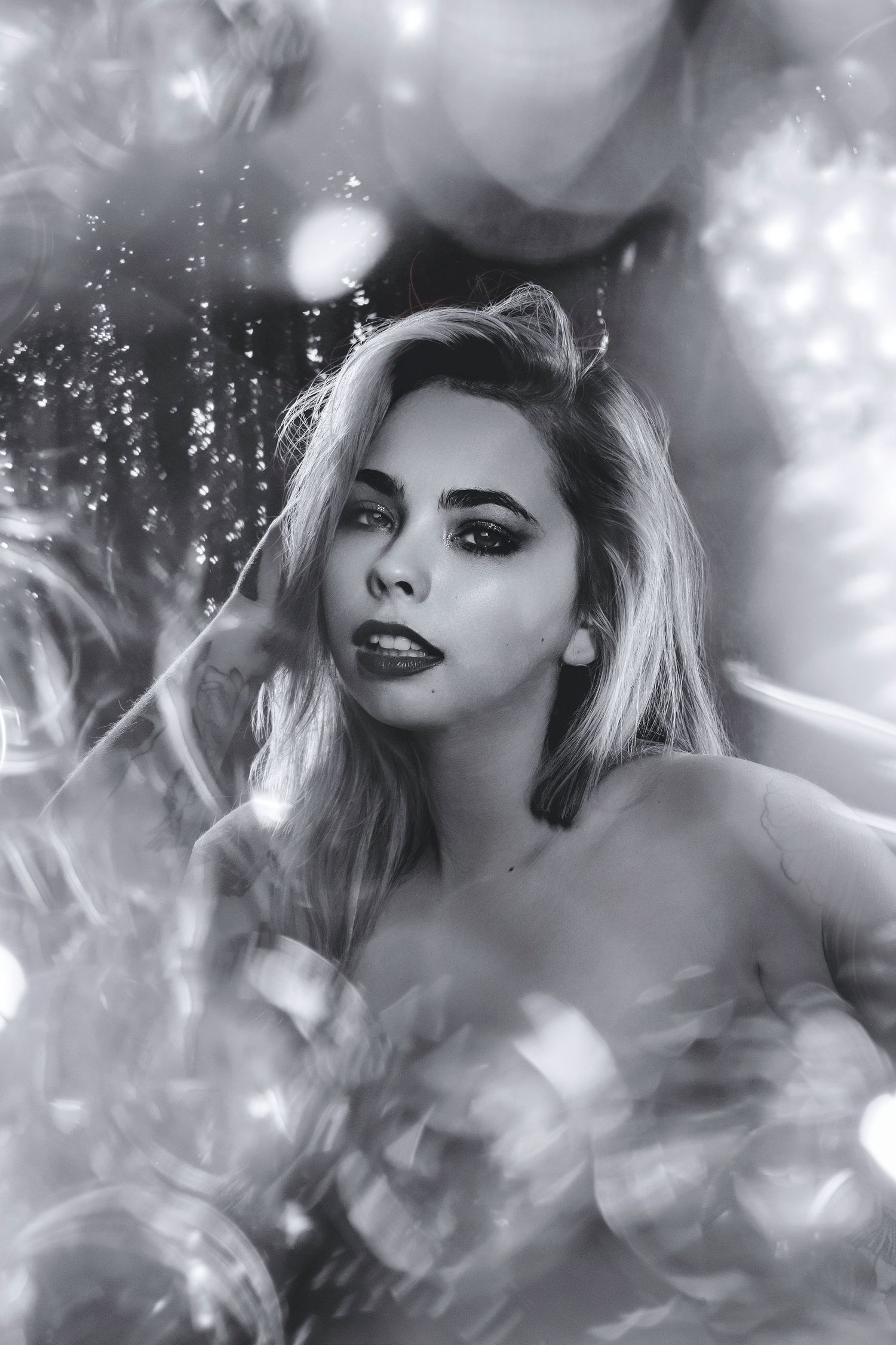 Black and white artistic portrait of blonde woman with dramatic makeup surrounded by bokeh balloons.