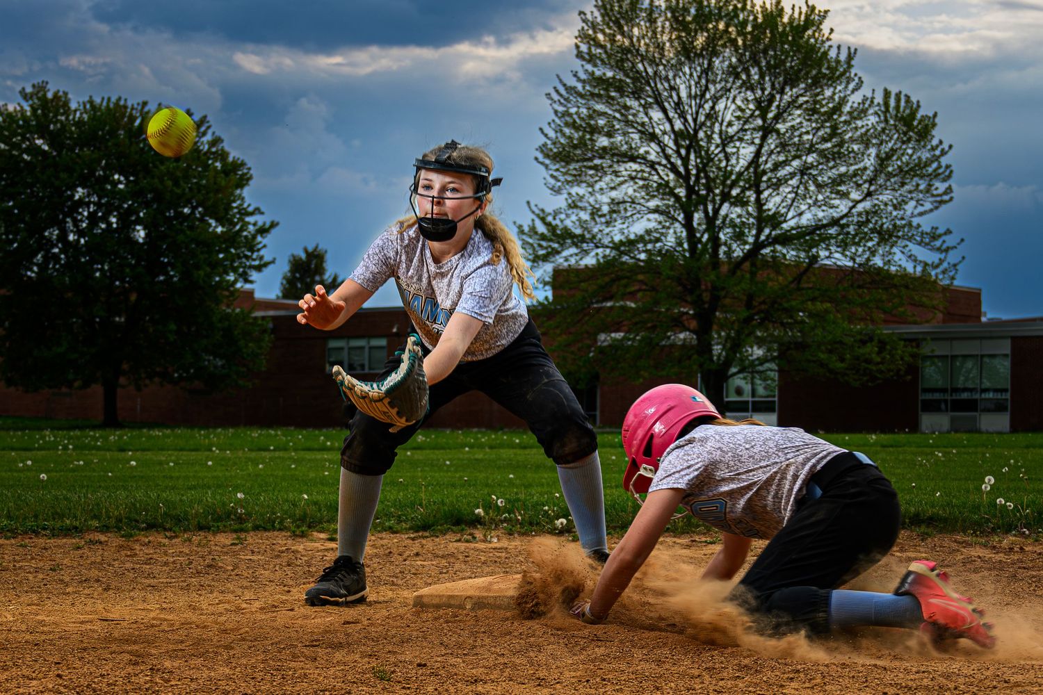 Two softball players in action, one fielding a throw while another slides into base in a dusty diamond.