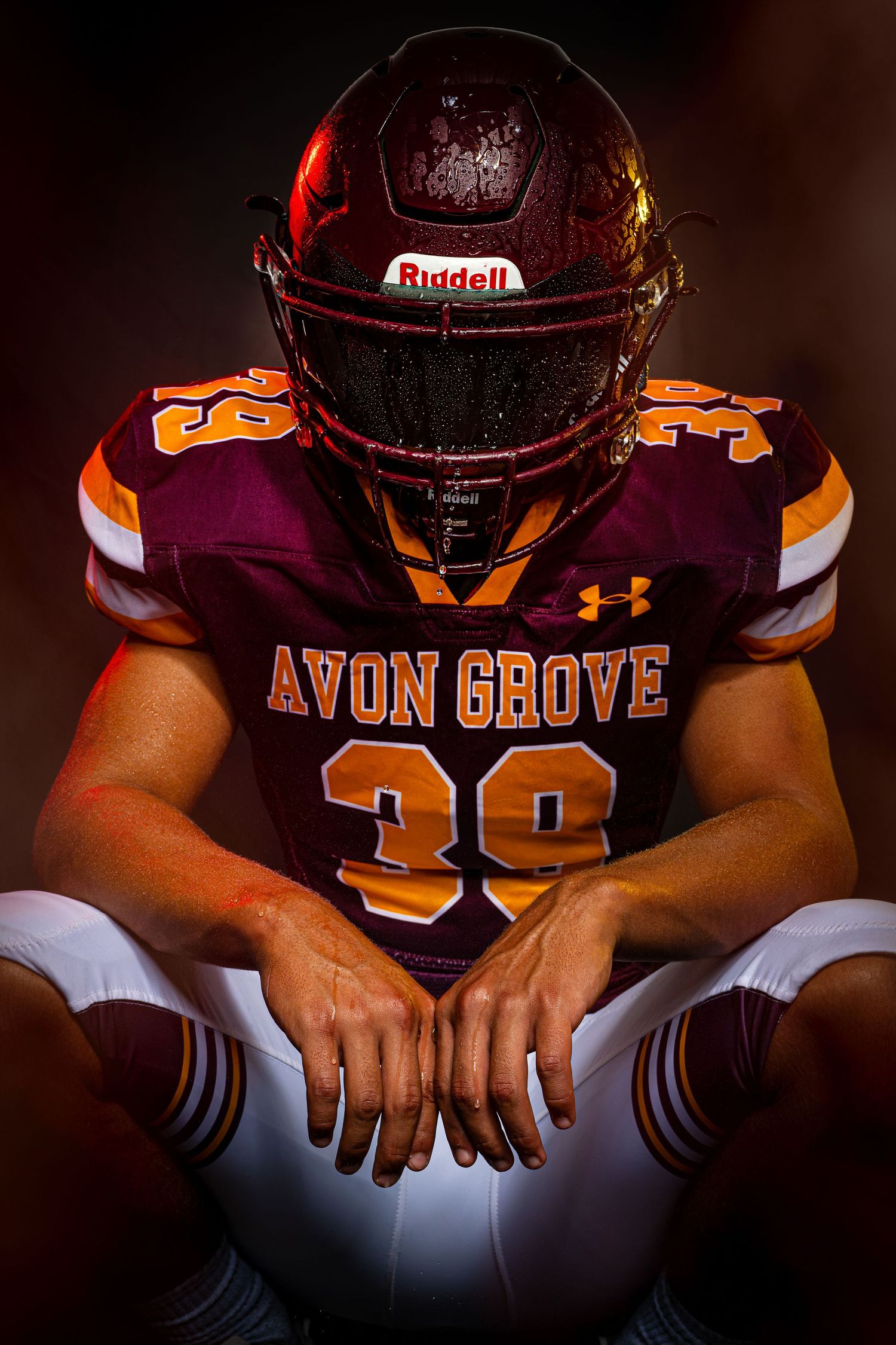 Avon Grove #39 football player sits head bowed in moody dark dramatic studio portrait.