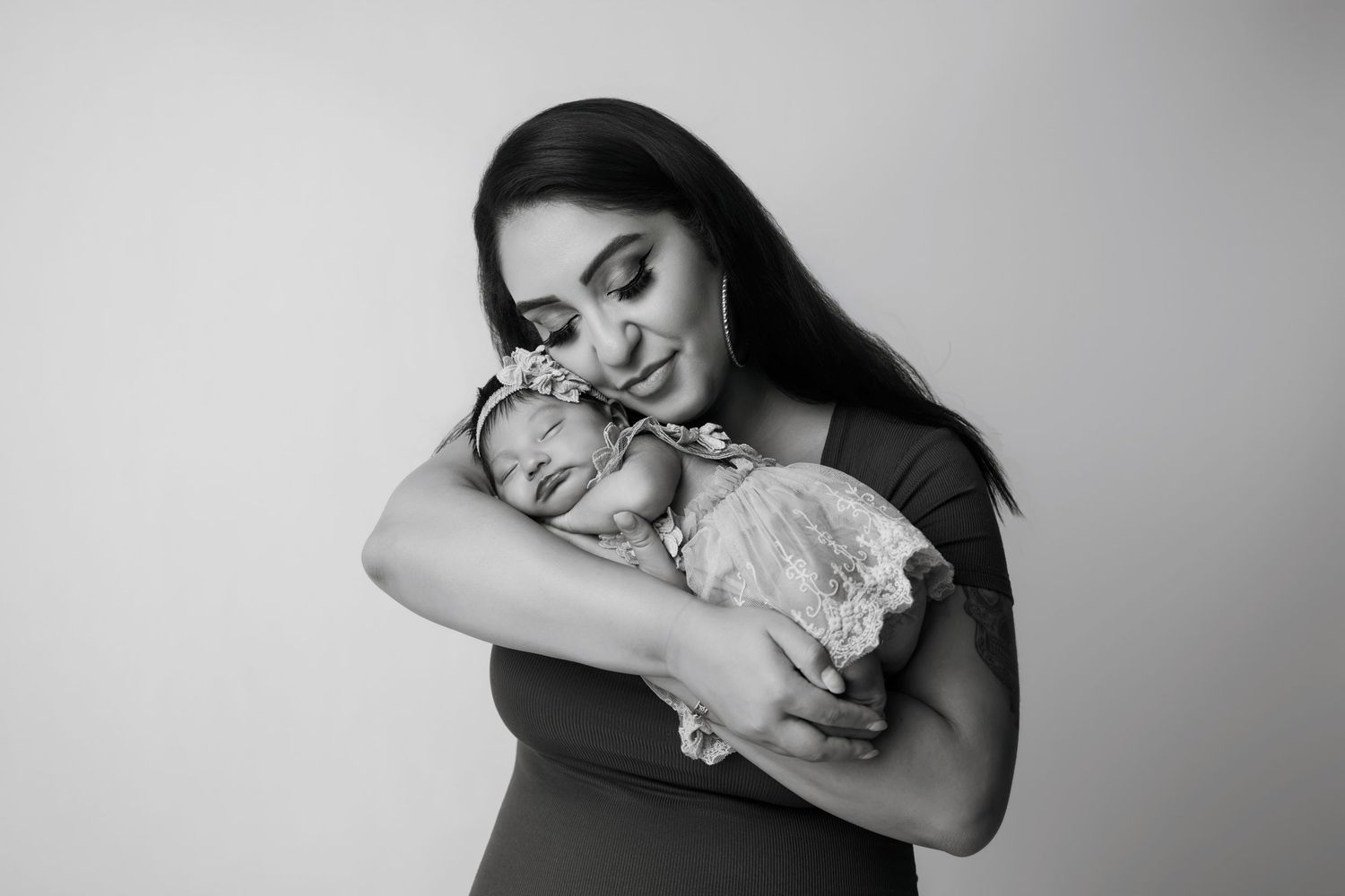 Black and white photo of a mother tenderly cradling her sleeping newborn baby close to her chest.