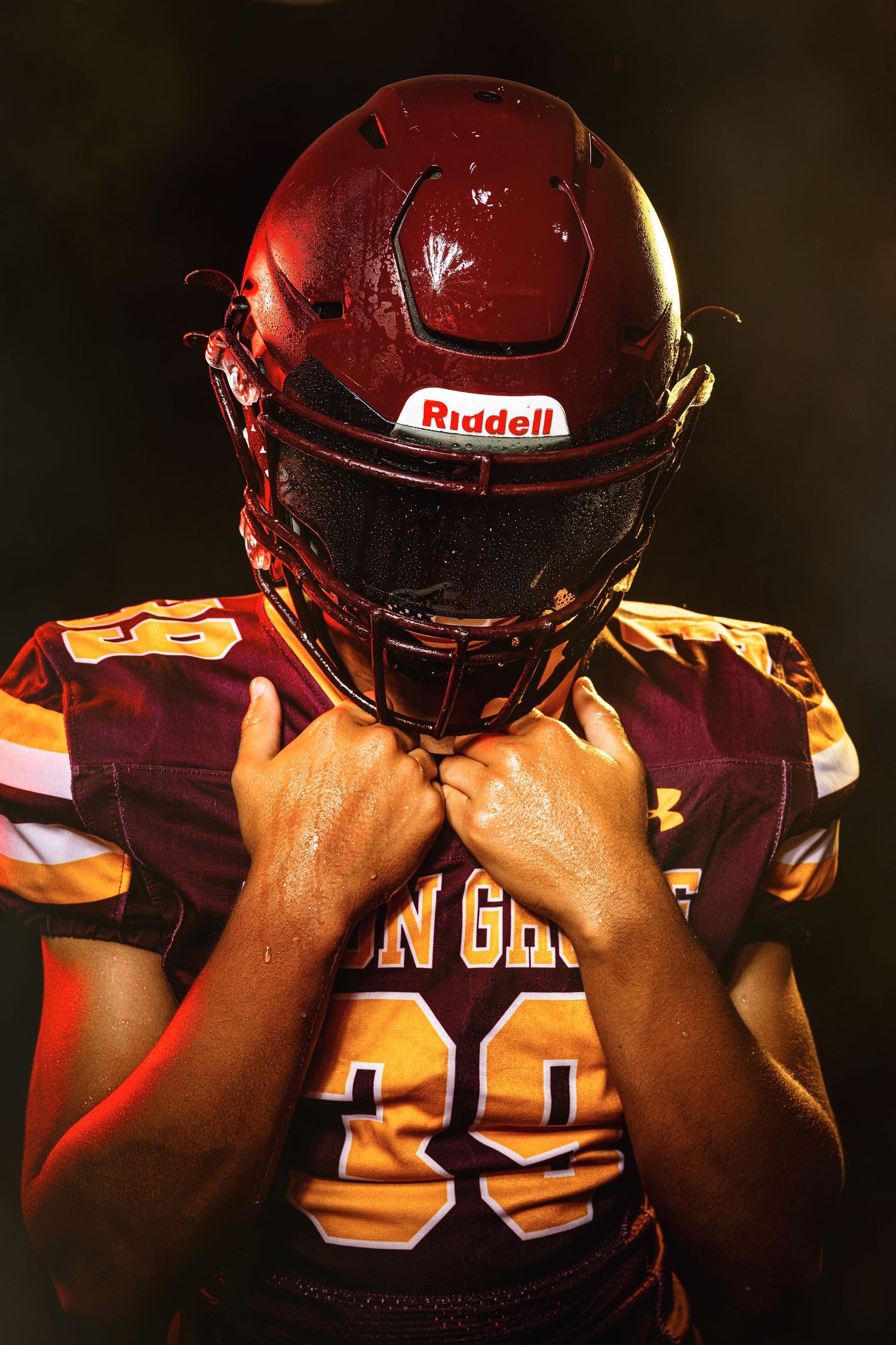 Avon Grove #39 player in wet Riddell helmet bows head in dramatic dark action portrait.