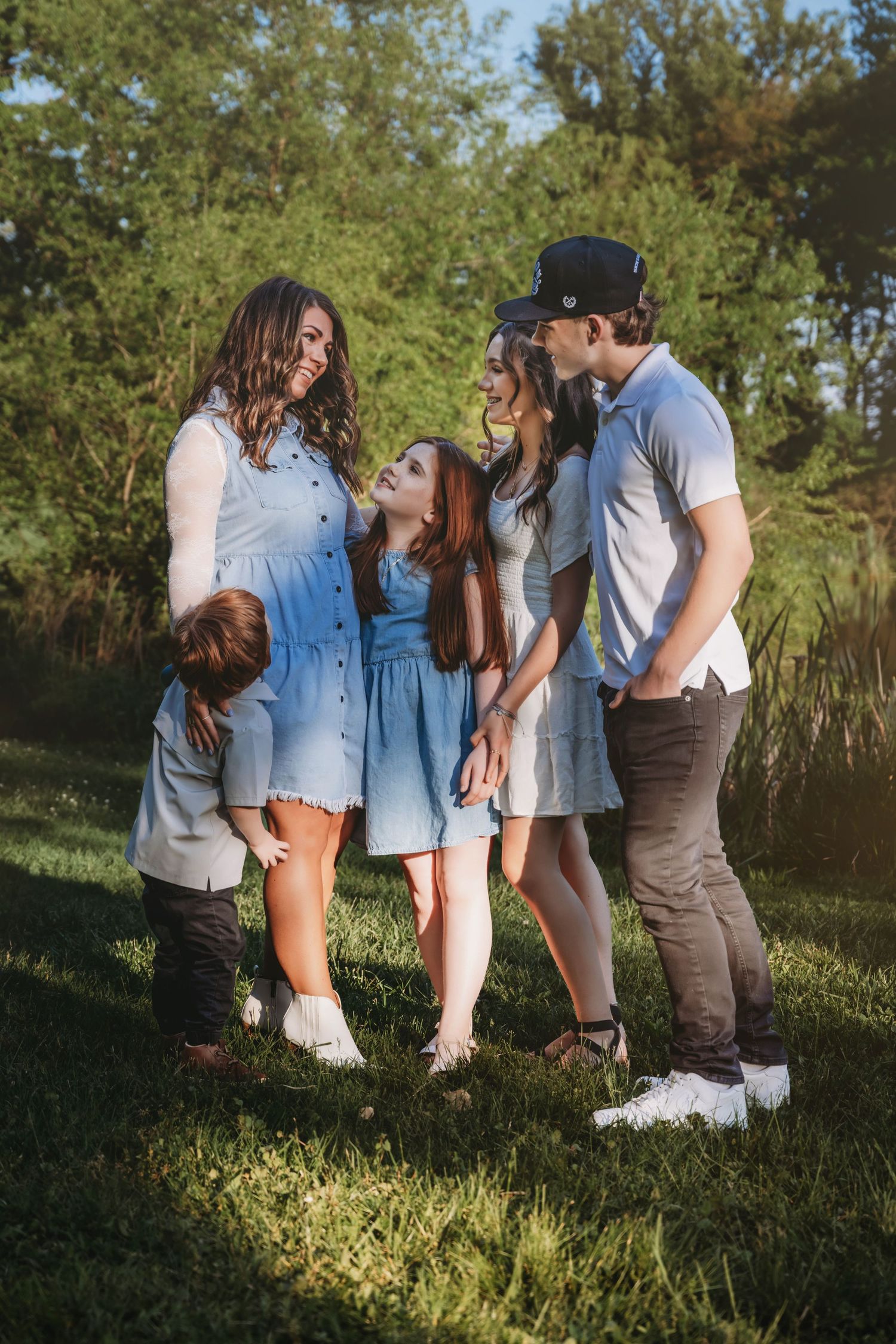 Happy family of five sharing a joyful moment outdoors on green grass surrounded by lush trees on a sunny day.