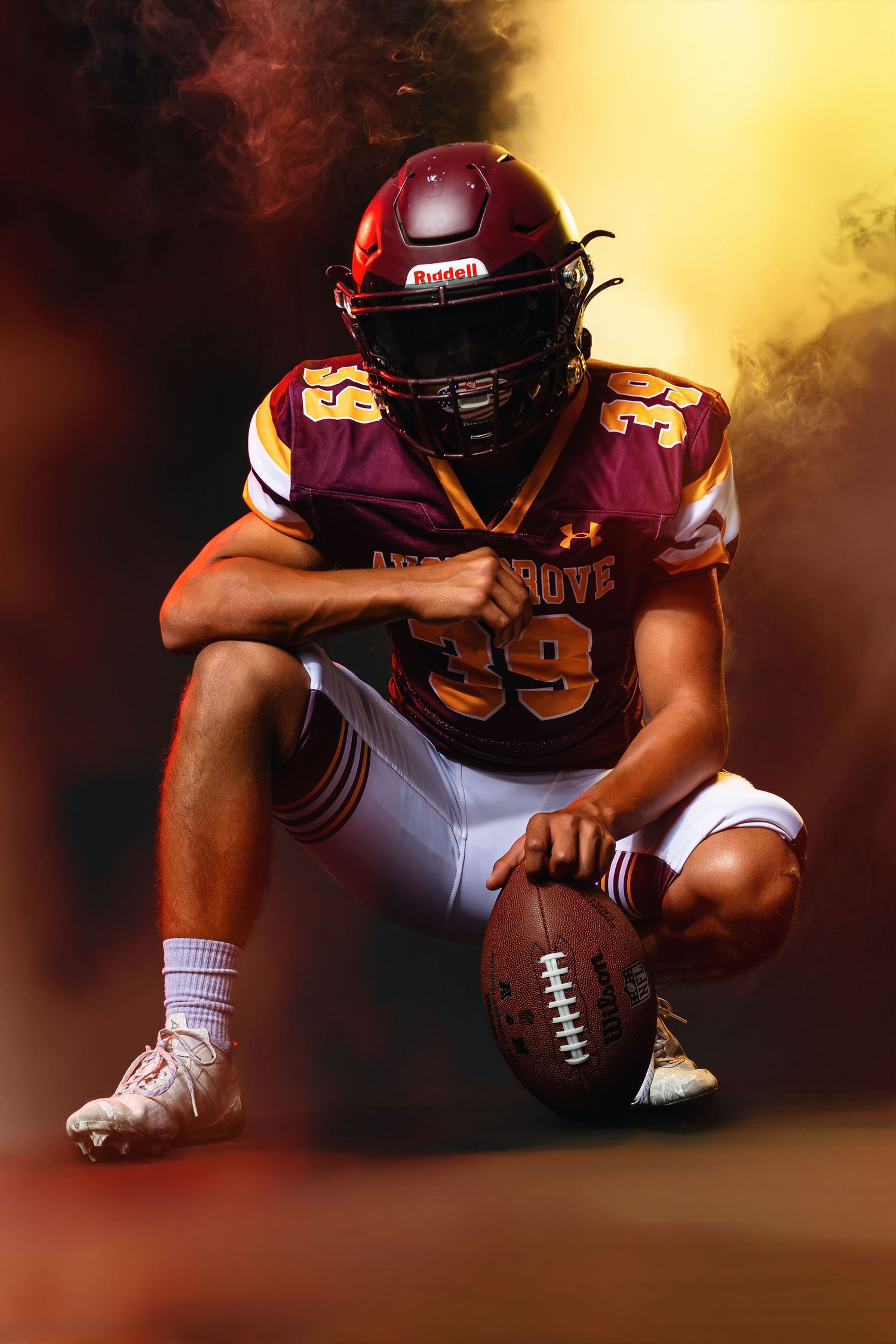 Avon Grove #39 football player crouches with ball in dramatic golden smoke studio portrait.