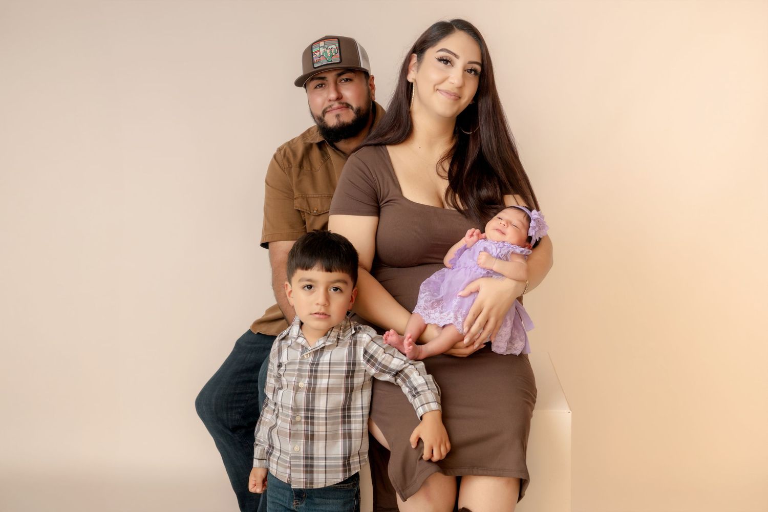 Family portrait with parents and two children, including a newborn baby, posing together in a studio setting.
